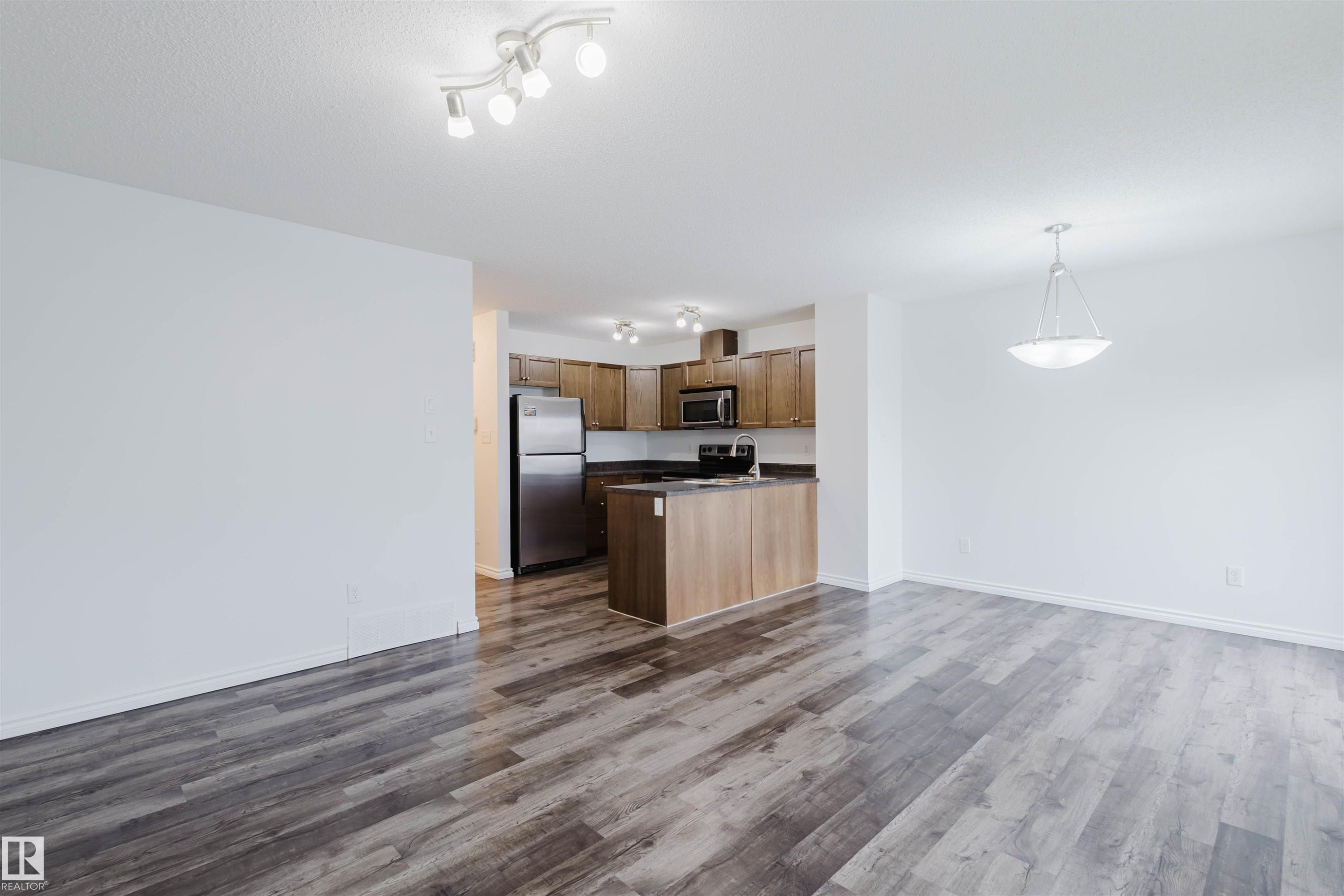 Kitchen featuring open floor plan, stainless steel appliances, dark countertops, hanging light fixtures, and dark wood finished floors - Edmonton, AB - Indoor Photo Showing Kitchen