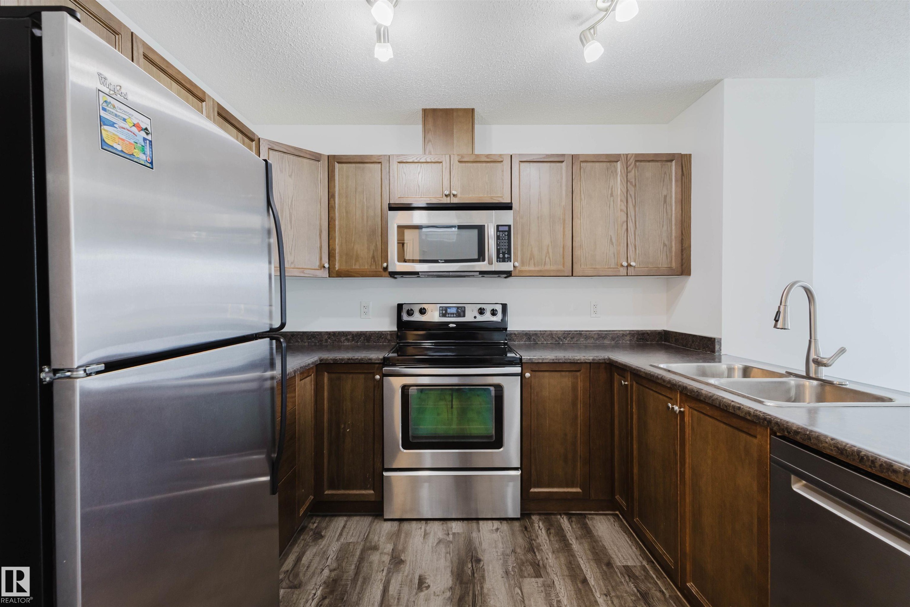 Kitchen with stainless steel appliances, dark countertops, a textured ceiling, and dark wood-style floors - Edmonton, AB - Indoor Photo Showing Kitchen With Stainless Steel Kitchen With Double Sink