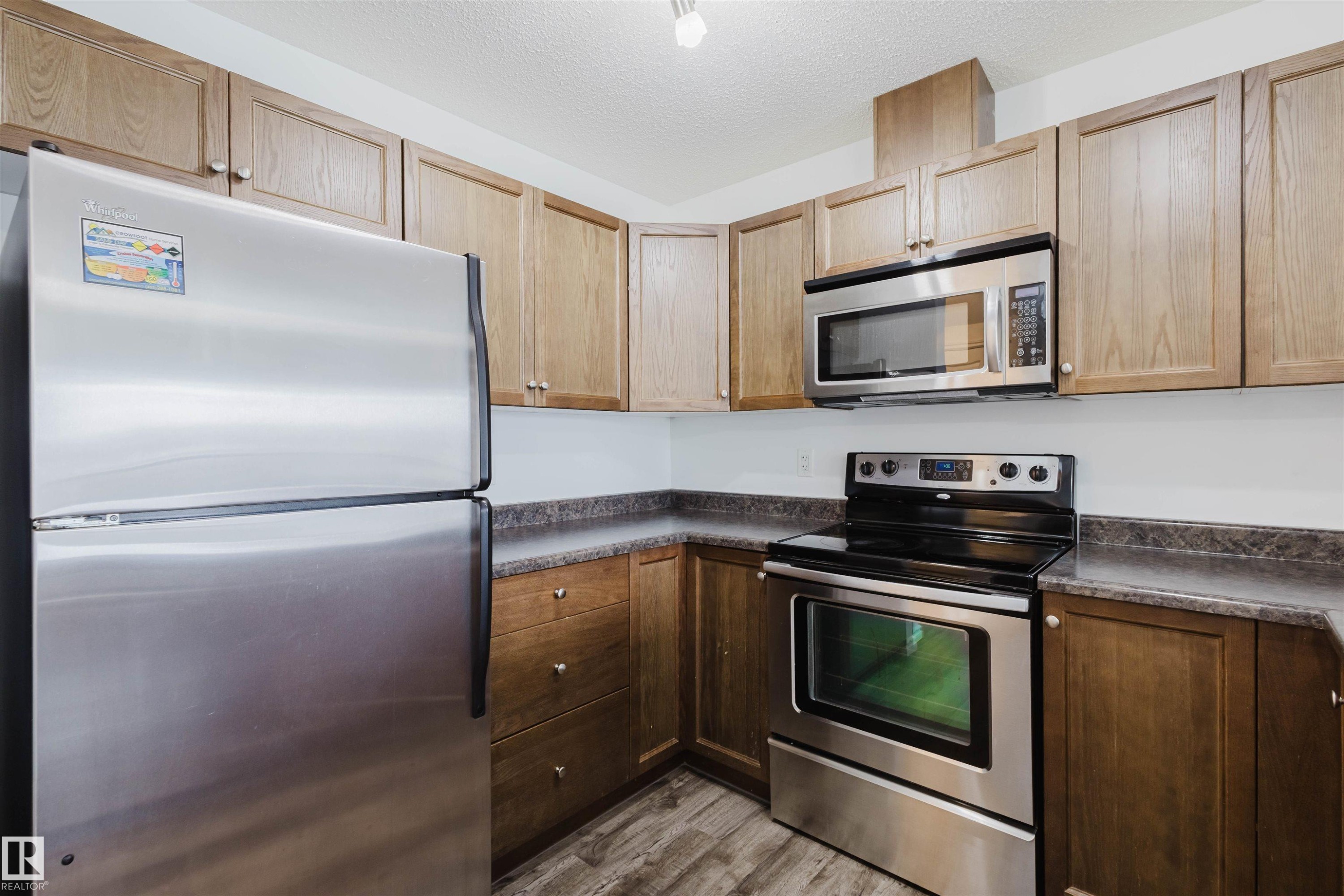 Kitchen featuring stainless steel appliances, dark countertops, a textured ceiling, and light wood finished floors - Edmonton, AB - Indoor Photo Showing Kitchen With Stainless Steel Kitchen
