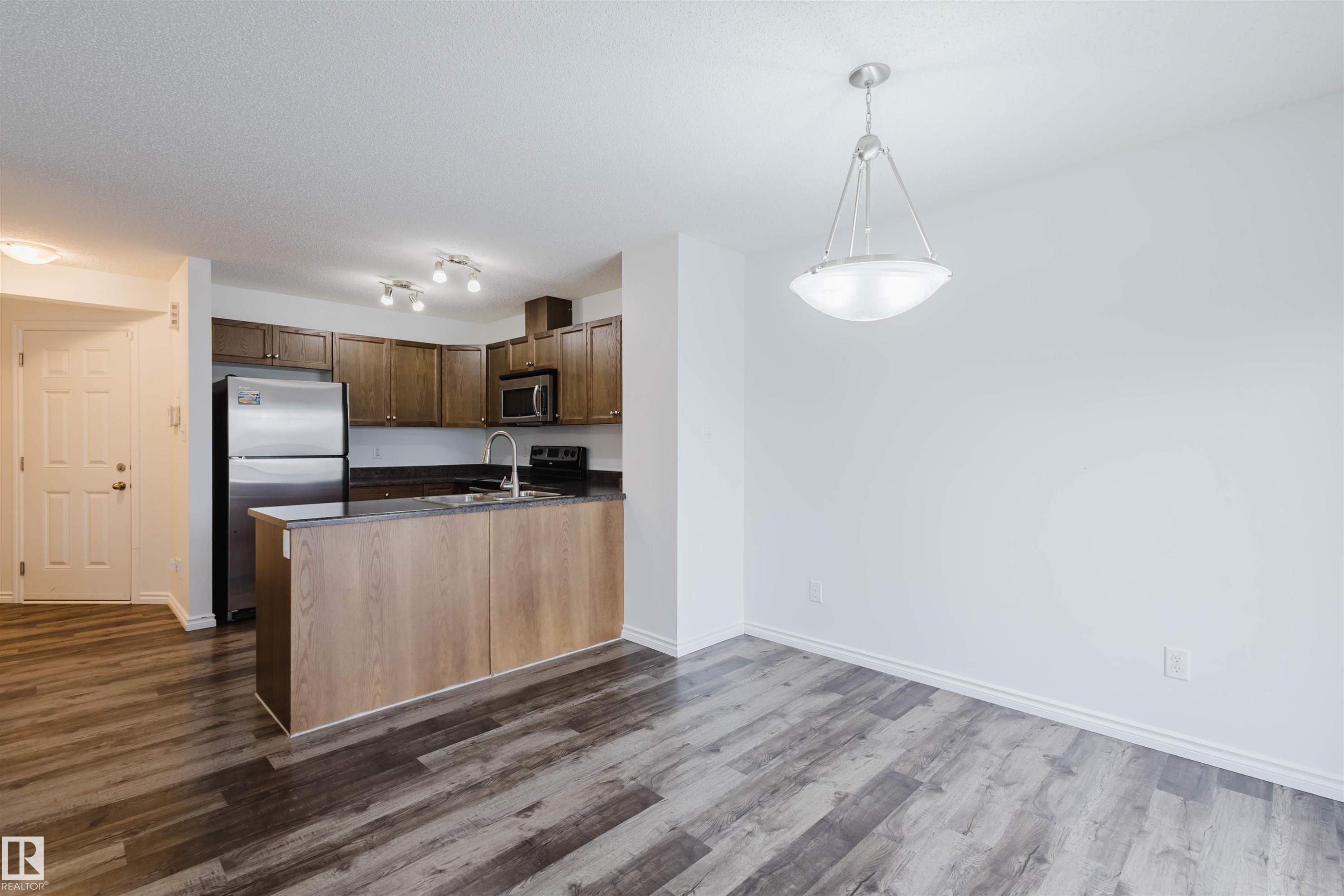 Kitchen featuring stainless steel appliances, dark countertops, hanging light fixtures, a peninsula, and dark wood-style flooring - Edmonton, AB - Indoor Photo Showing Kitchen