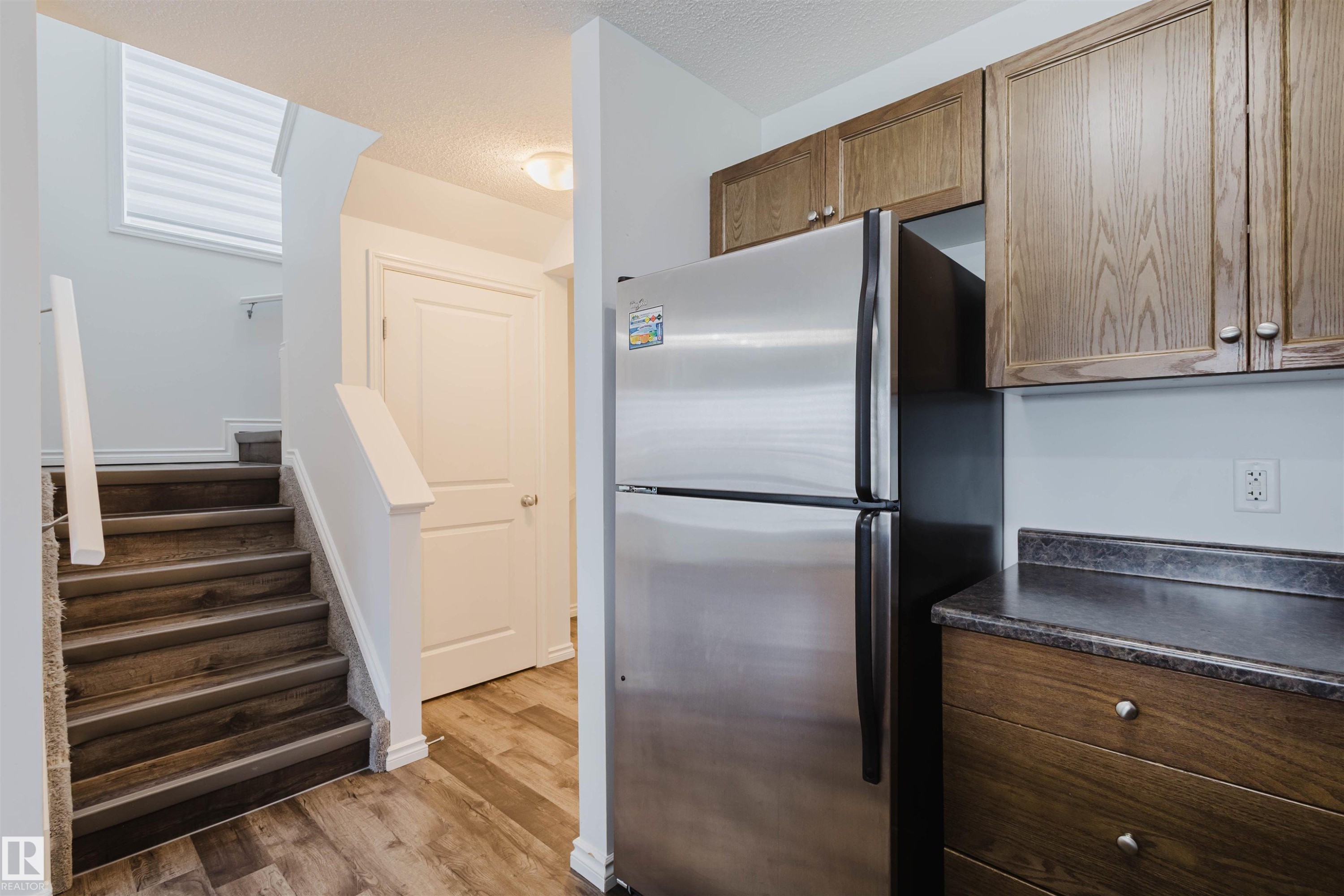 Kitchen with dark countertops, freestanding refrigerator, dark wood-style flooring, a textured ceiling, and wood finish cabinetry - Edmonton, AB - Indoor