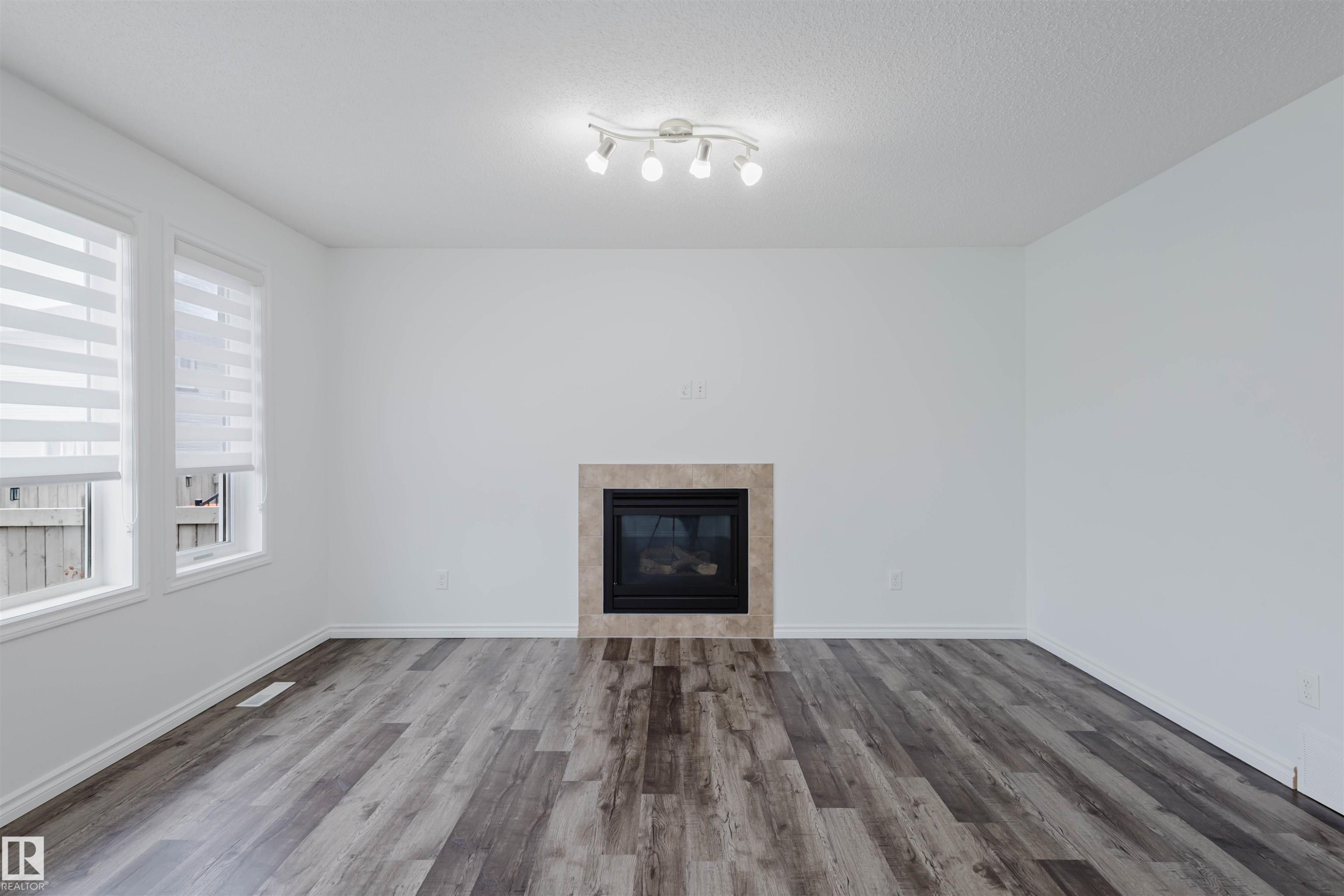 Unfurnished living room featuring a tiled fireplace and dark wood-type flooring - Edmonton, AB - Indoor Photo Showing Living Room With Fireplace