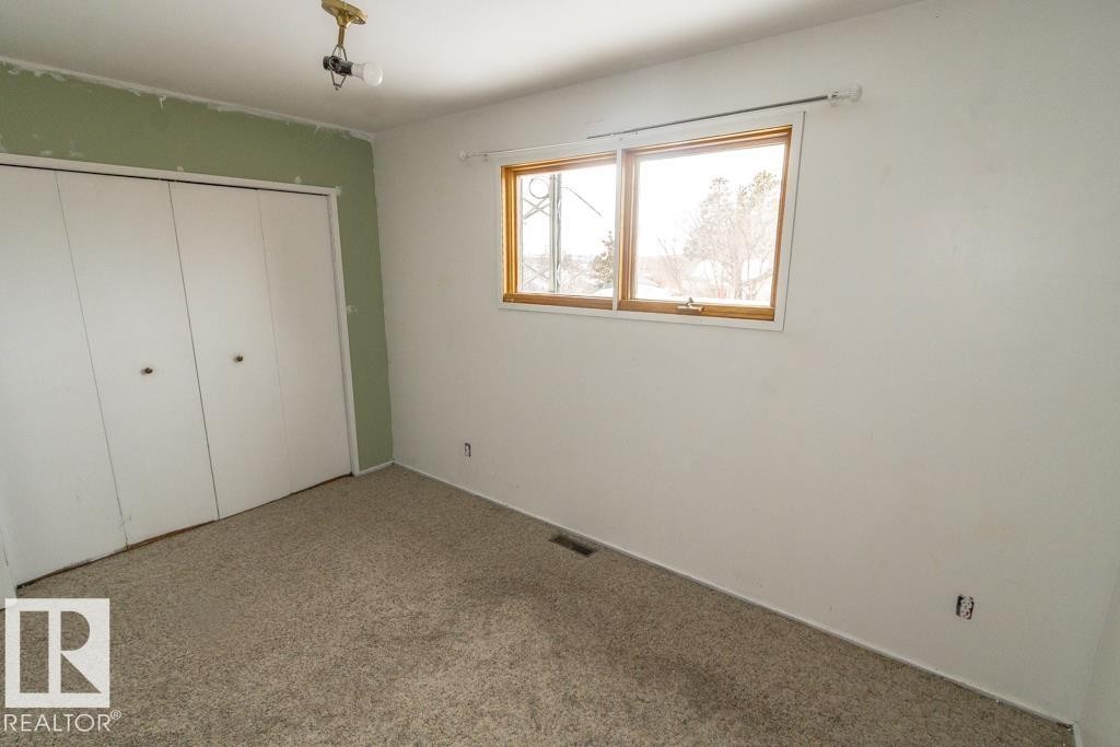 This room features a window with wood trim, a carpeted floor, and a closet with bifold doors - 5016 47 St, Myrnam, AB - Indoor Photo Showing Other Room