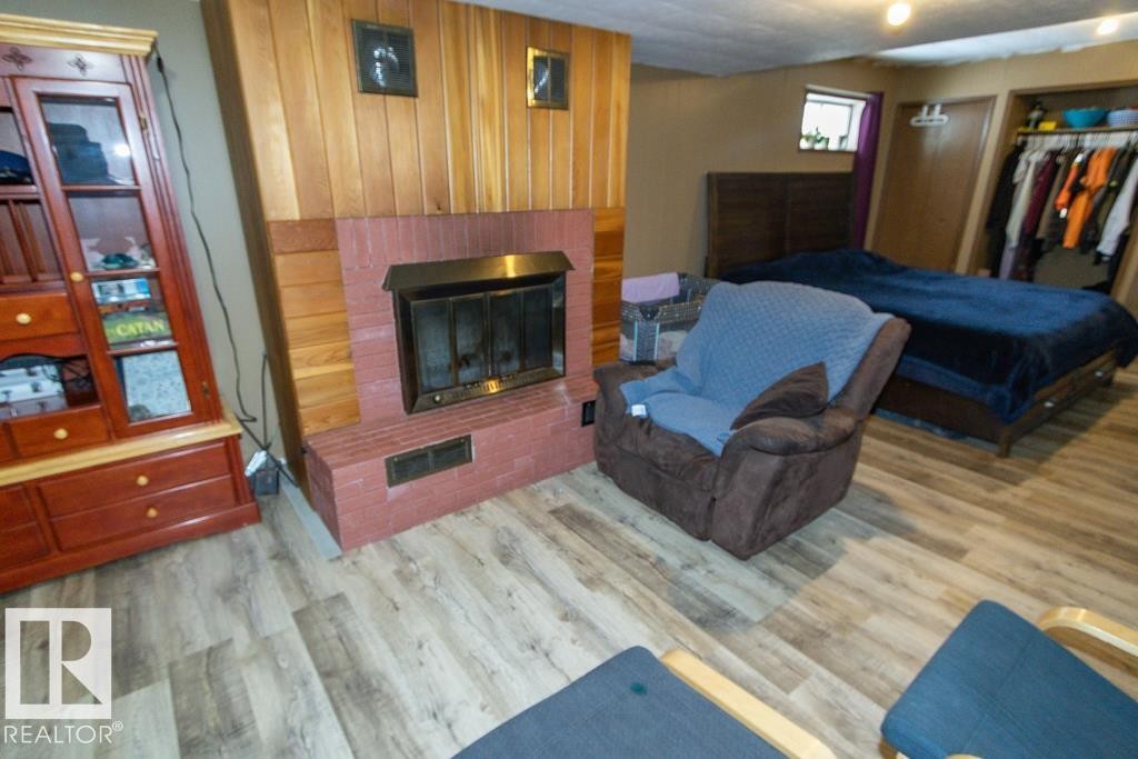 This inviting space features a brick fireplace with a wood panel accent wall, durable wood-look flooring, and a window providing natural light - 5016 47 St, Myrnam, AB - Indoor