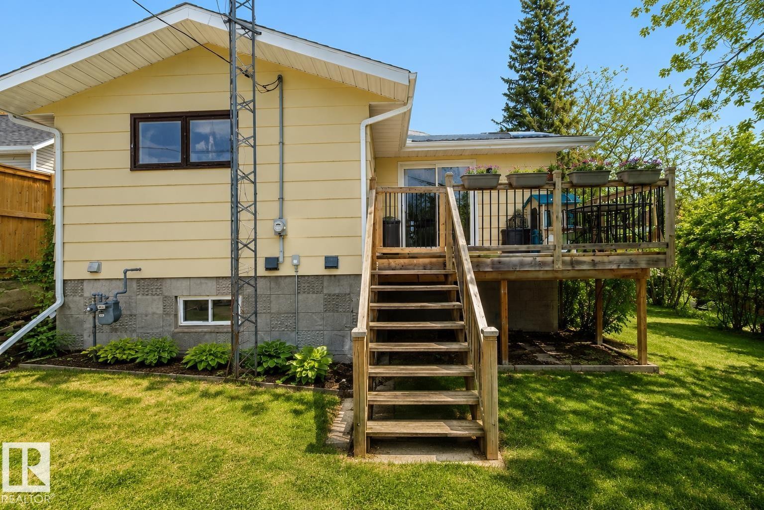Backyard featuring a wooden deck with black railings, exterior stairs, and a sliding glass door - 5016 47 St, Myrnam, AB - Outdoor