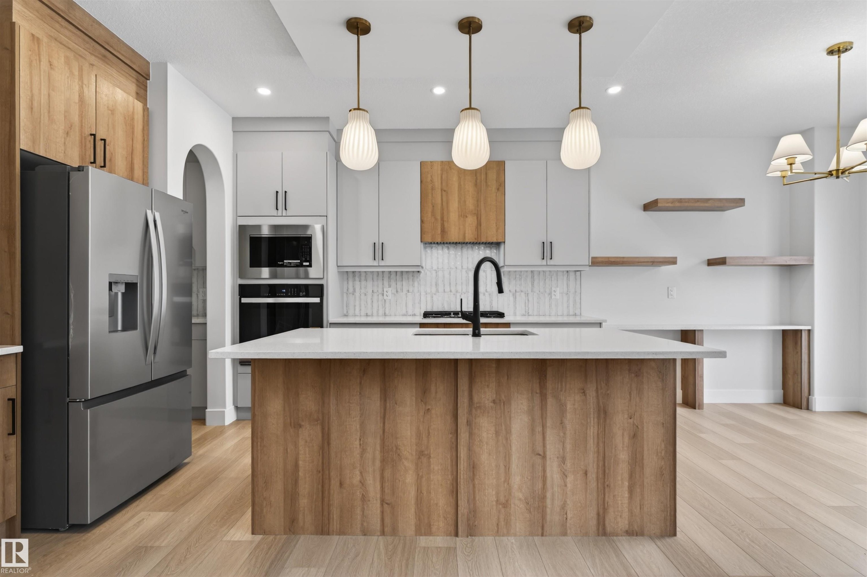 Well-appointed kitchen featuring a large island with a white countertop, modern pendant lighting, and stainless steel appliances - 11 Redbud Way, St. Albert, AB - Indoor Photo Showing Kitchen With Upgraded Kitchen