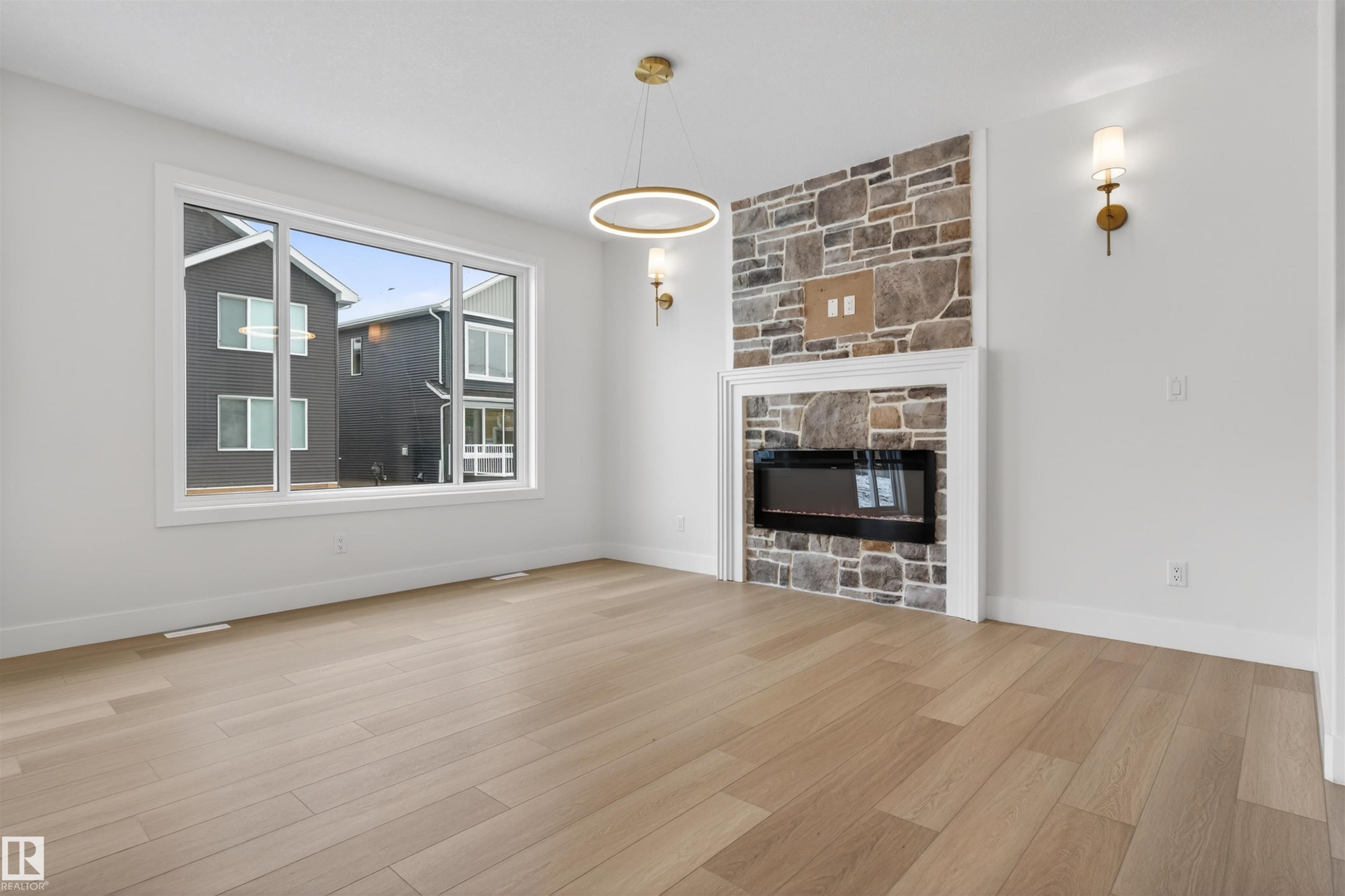 This inviting room features light-toned wood flooring, an electric fireplace with a stone surround, and a large window providing natural light - 11 Redbud Way, St. Albert, AB - Indoor Photo Showing Living Room With Fireplace