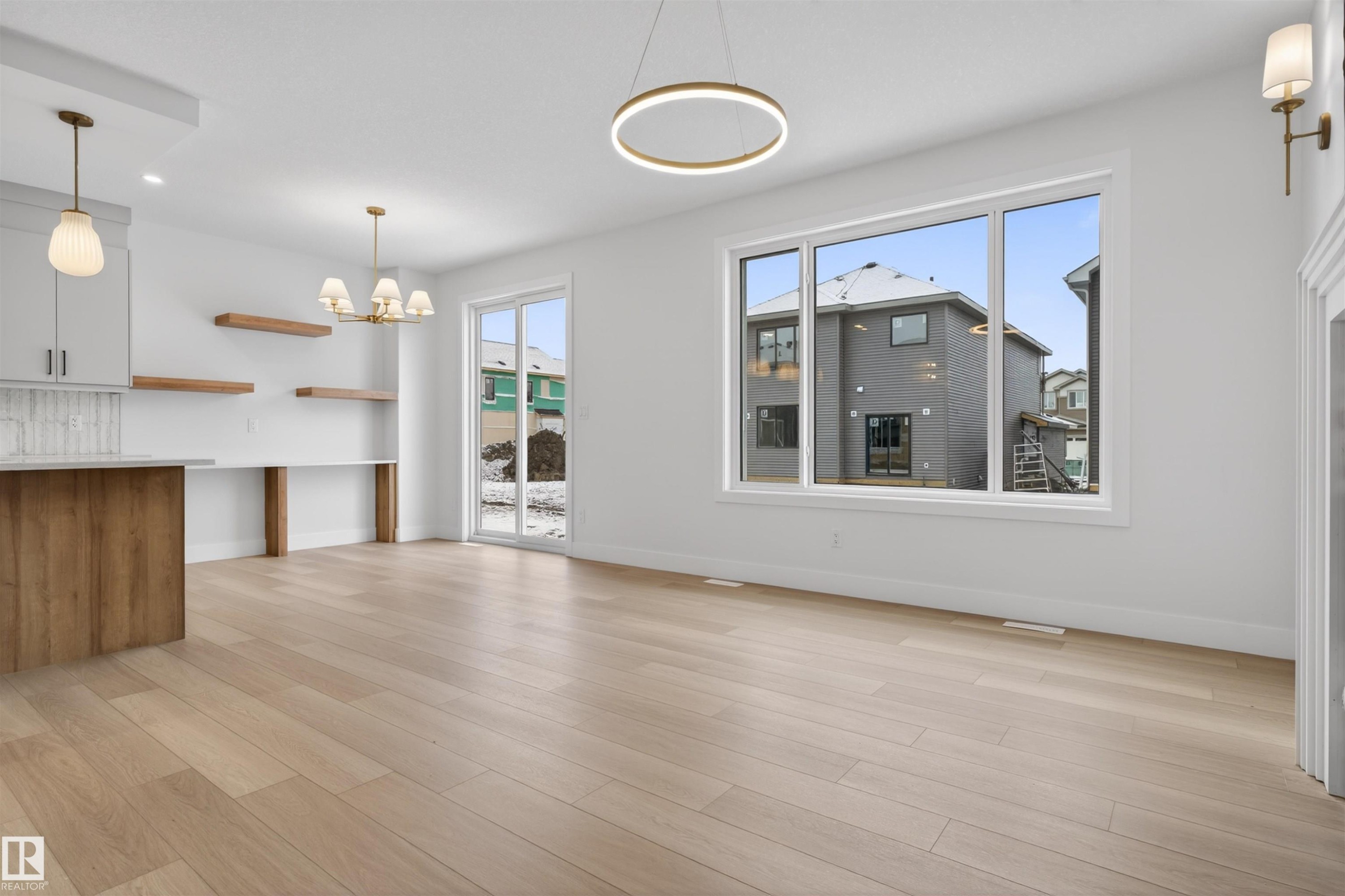 Spacious open concept room featuring light-colored hardwood floors, large windows providing natural light, and modern light fixtures - 11 Redbud Way, St. Albert, AB - Indoor