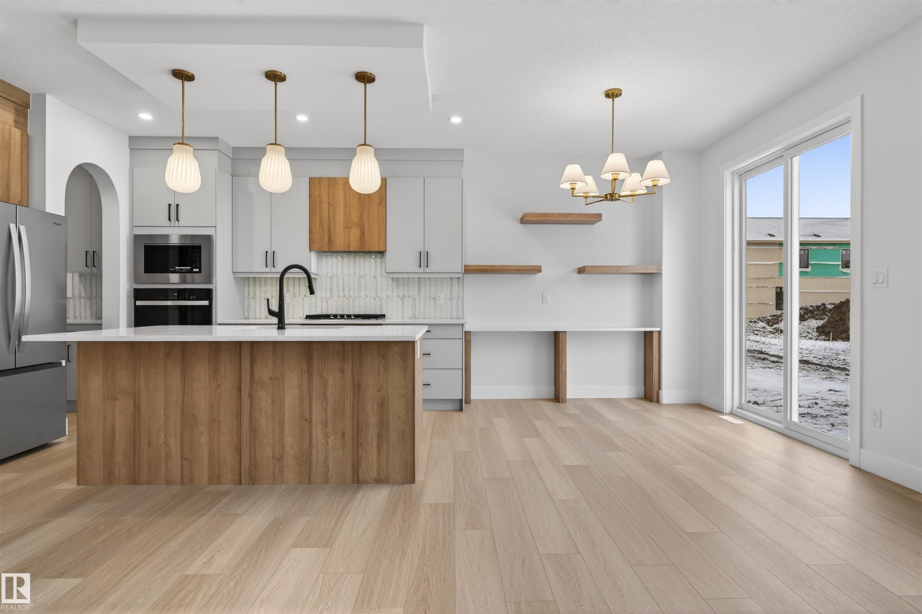 This kitchen features a central island with a wood-look base, a white countertop, and three pendant lights overhead - 11 Redbud Way, St. Albert, AB - Indoor Photo Showing Kitchen With Upgraded Kitchen