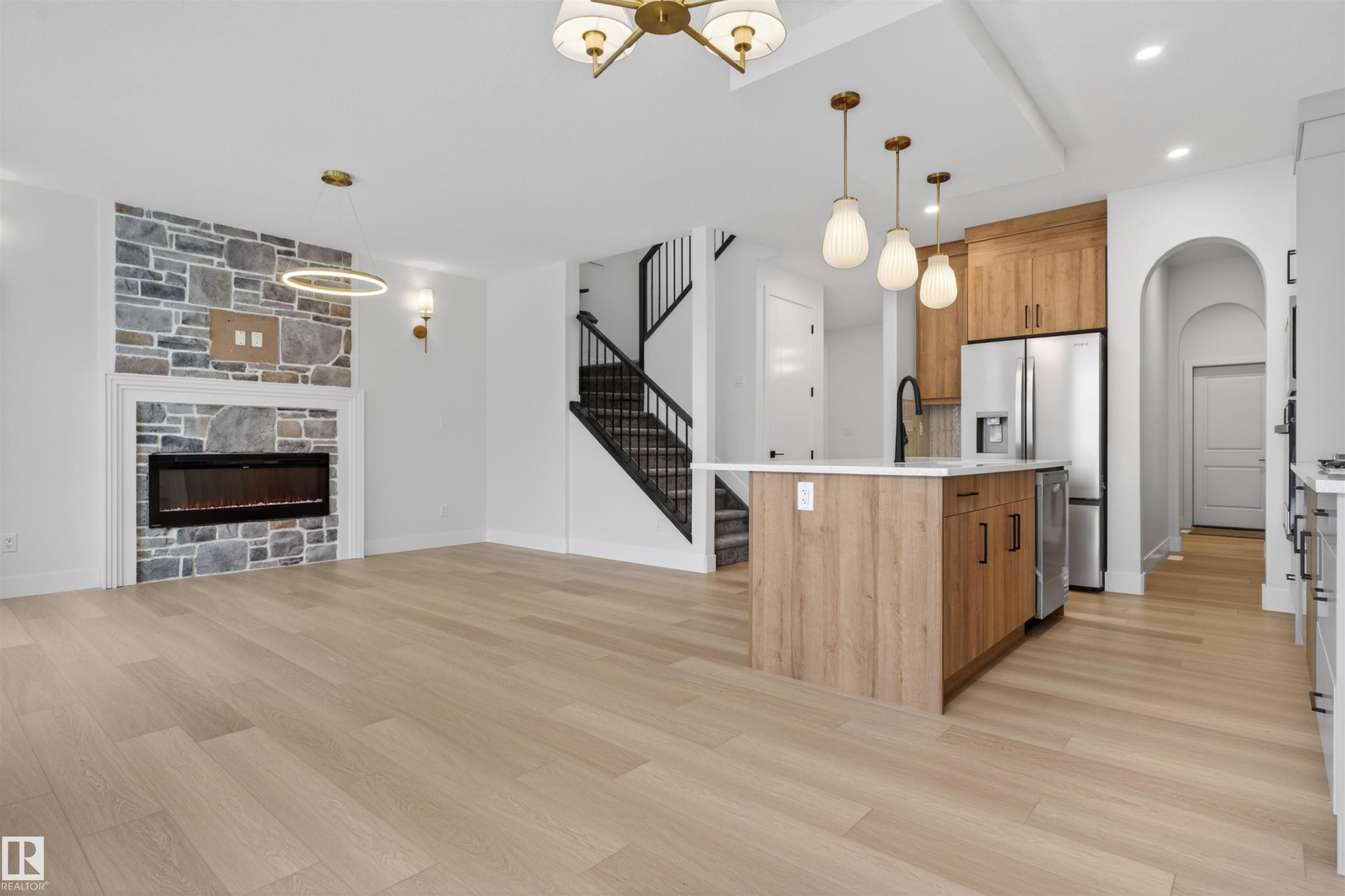 This open-concept living space features light-toned wood flooring, a stone-faced fireplace, and a kitchen island with pendant lighting - 11 Redbud Way, St. Albert, AB - Indoor Photo Showing Kitchen With Fireplace With Upgraded Kitchen
