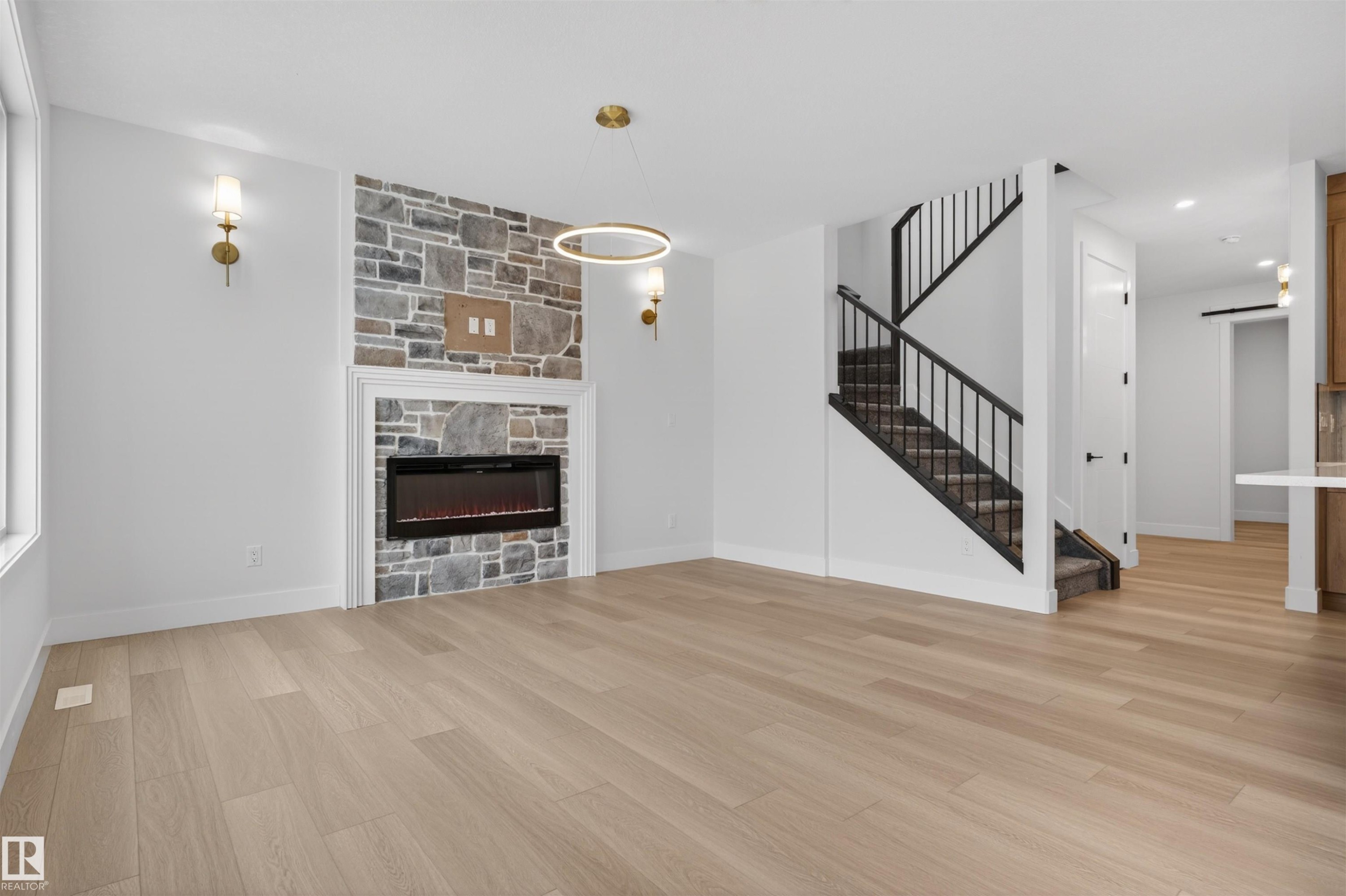 This property features light-colored hardwood flooring throughout, a stone-clad fireplace with an electric insert, and a staircase with black railings - 11 Redbud Way, St. Albert, AB - Indoor With Fireplace