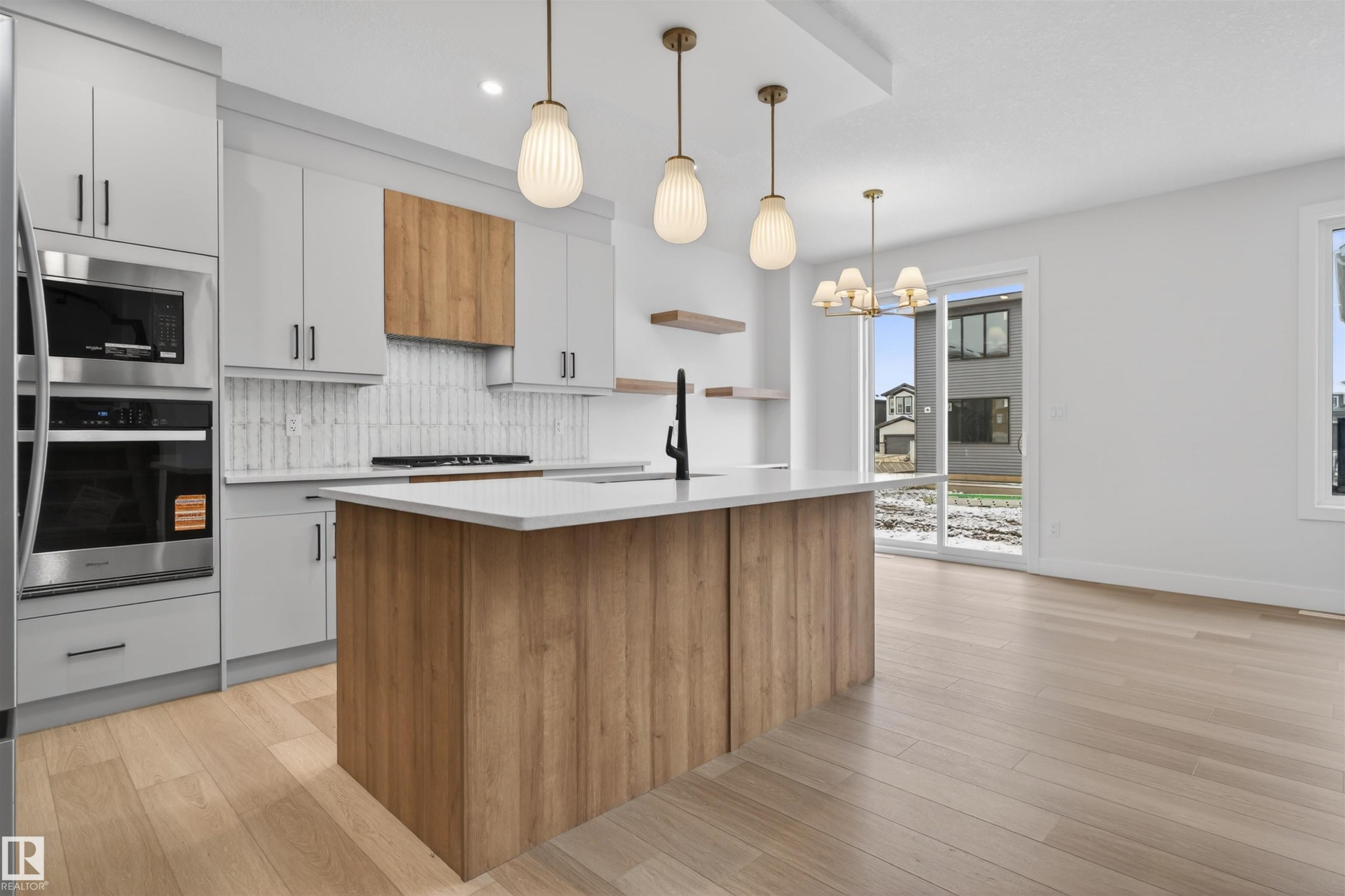 Open-concept kitchen and living area featuring hardwood floors, a kitchen island with a light-colored countertop, and stainless steel appliances - 11 Redbud Way, St. Albert, AB - Indoor Photo Showing Kitchen With Upgraded Kitchen