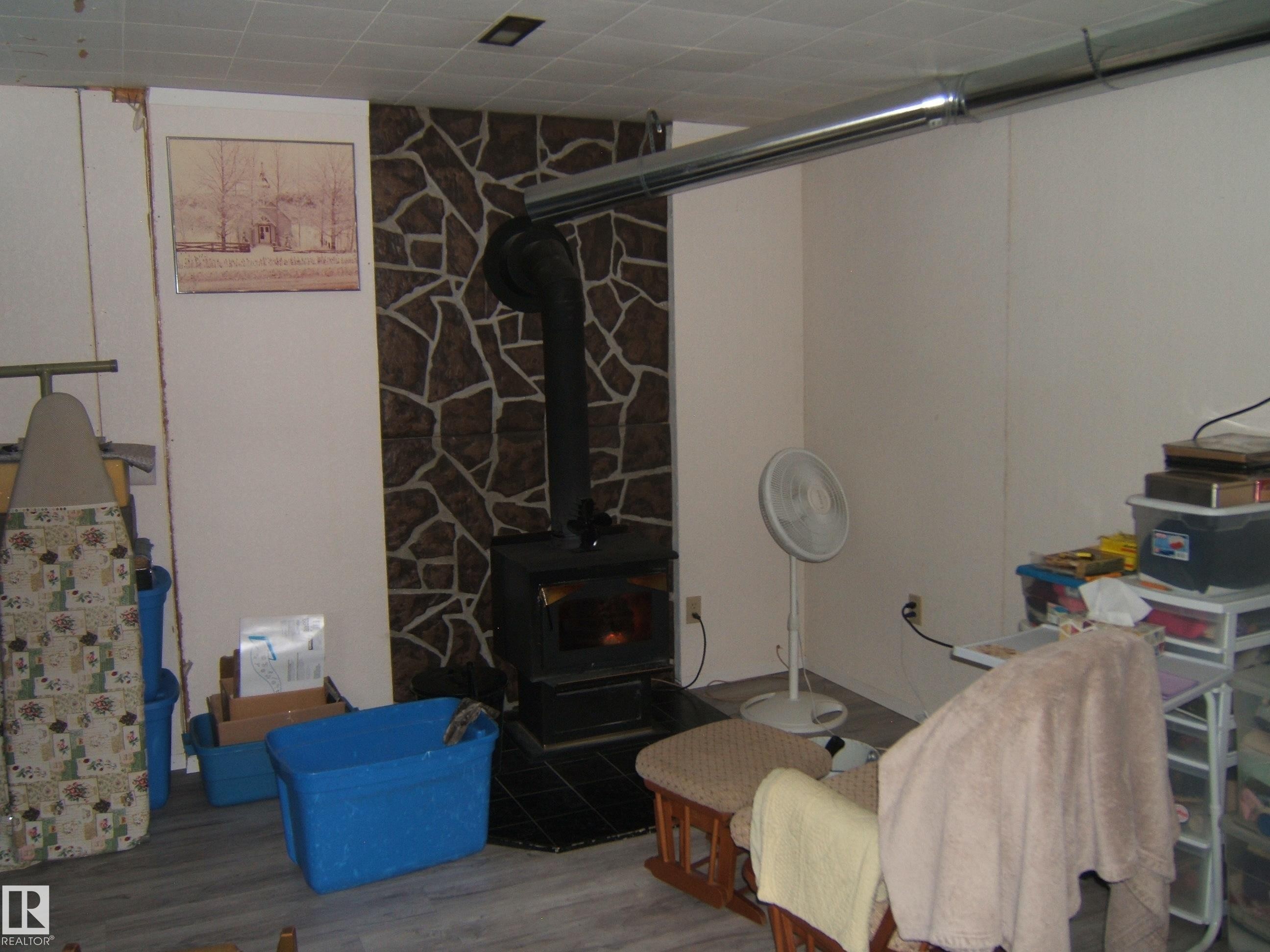The room features a wood-burning stove with a stone-accented wall and a grey floor - 4702 52 Avenue, Two Hills, AB - Indoor