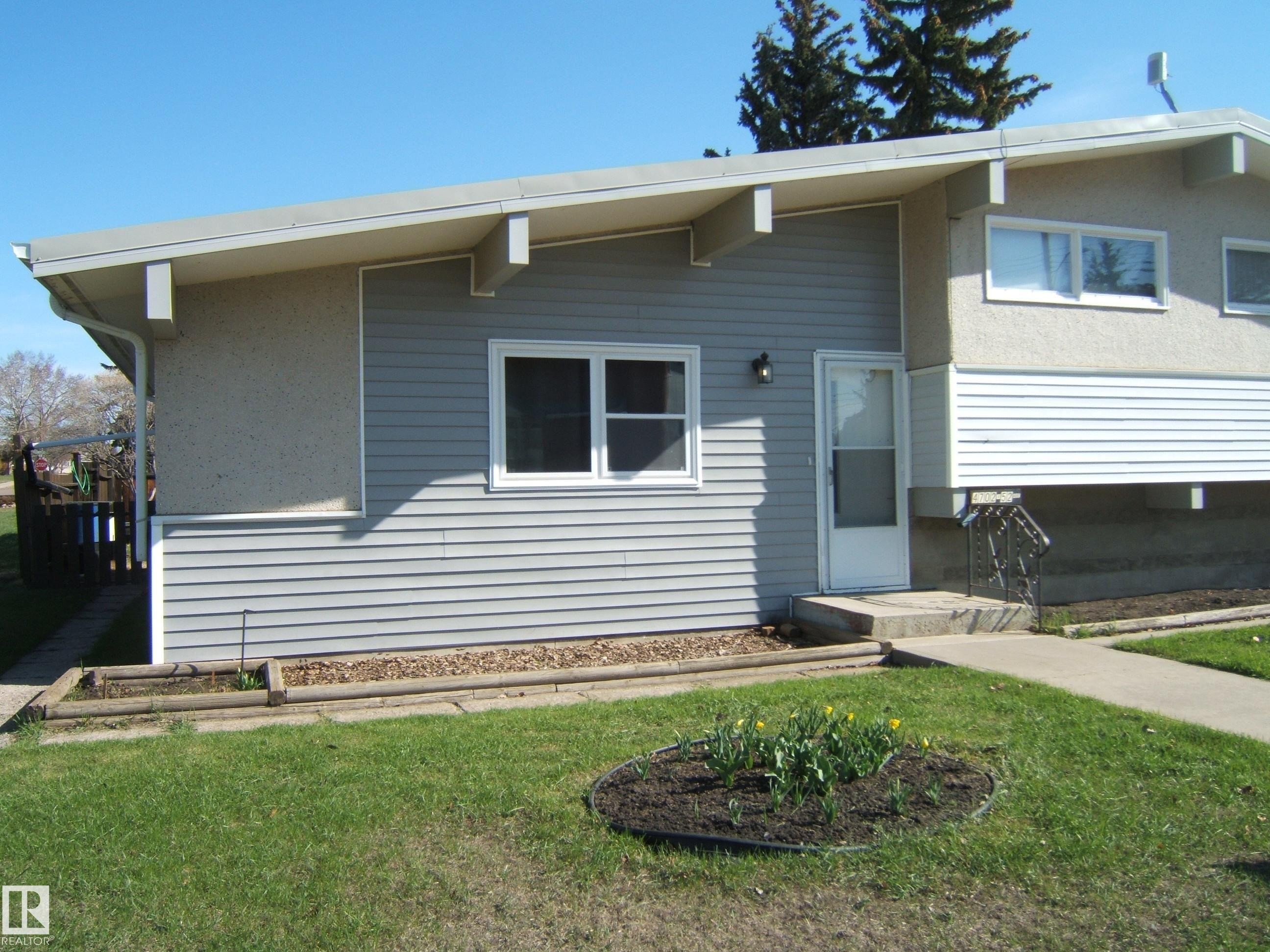Split-level exterior featuring light gray horizontal siding, stucco elements, white window trim, and a concrete front walkway - 4702 52 Avenue, Two Hills, AB - Outdoor With Exterior