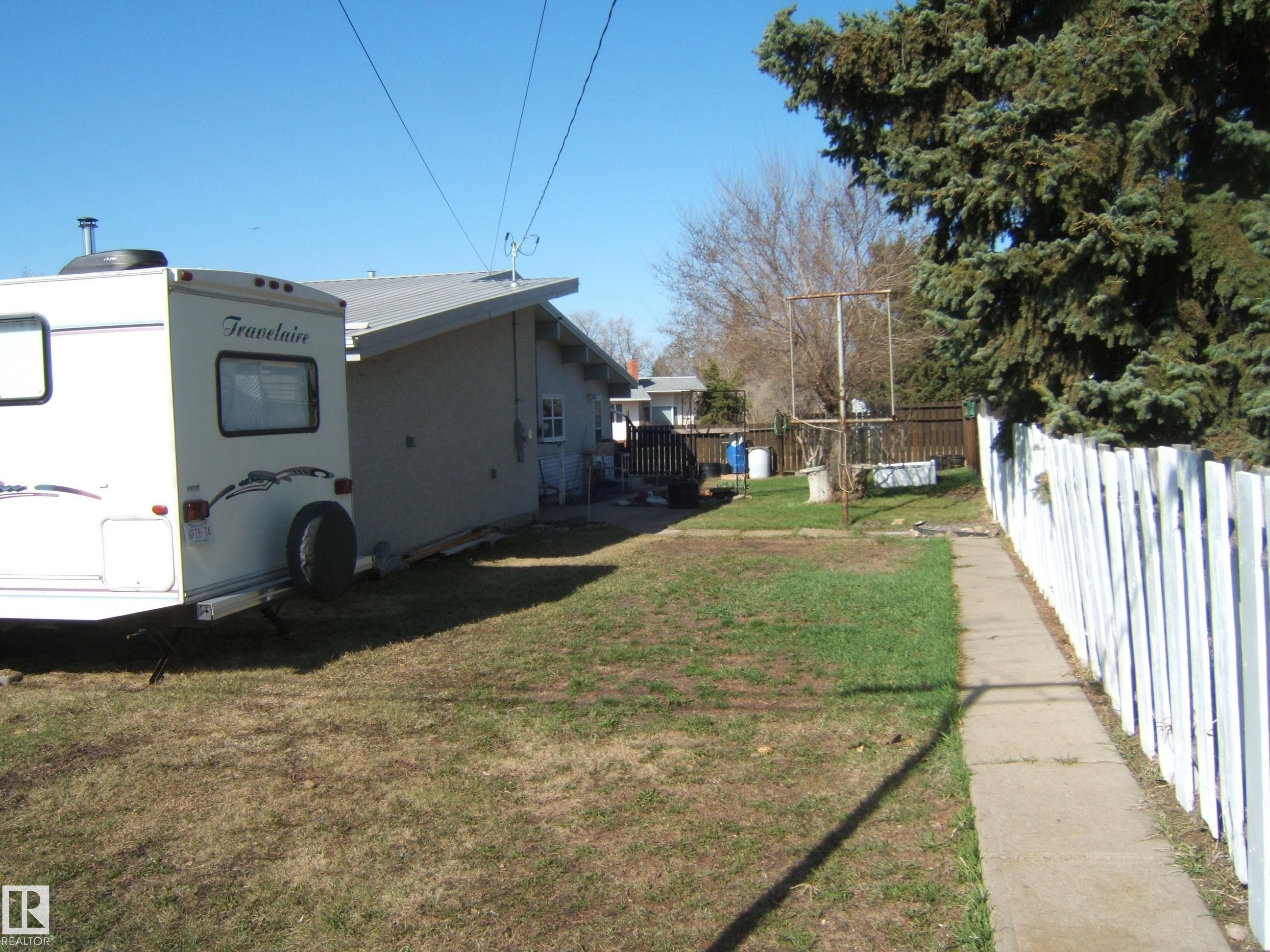 Rear exterior featuring a pitched roof, white picket fence, and concrete pathway - 4702 52 Avenue, Two Hills, AB - Outdoor