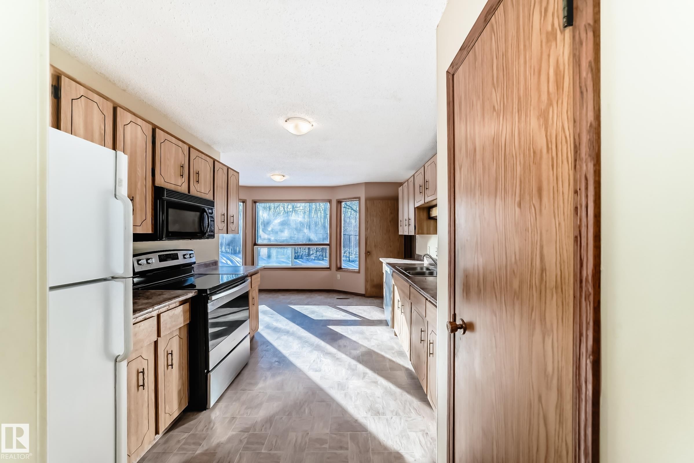 The kitchen features light wood cabinetry, black appliances, and a window with a view of the outdoors - 100 23016 Twp Rd 504, Rural Leduc County, AB - Indoor Photo Showing Kitchen
