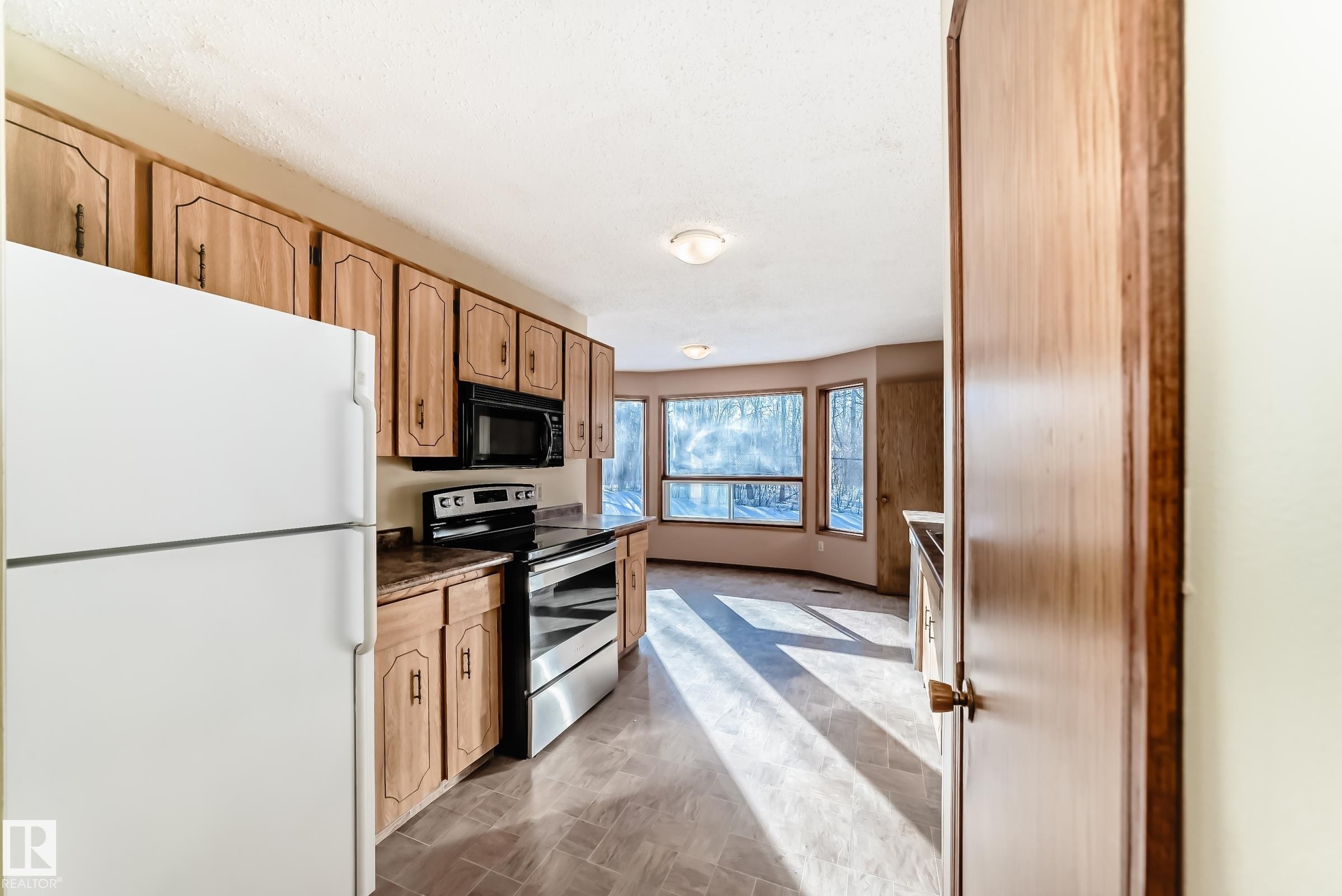 The kitchen features light wood cabinetry, a white refrigerator, a black microwave, and a stainless steel oven and range - 100 23016 Twp Rd 504, Rural Leduc County, AB - Indoor Photo Showing Kitchen