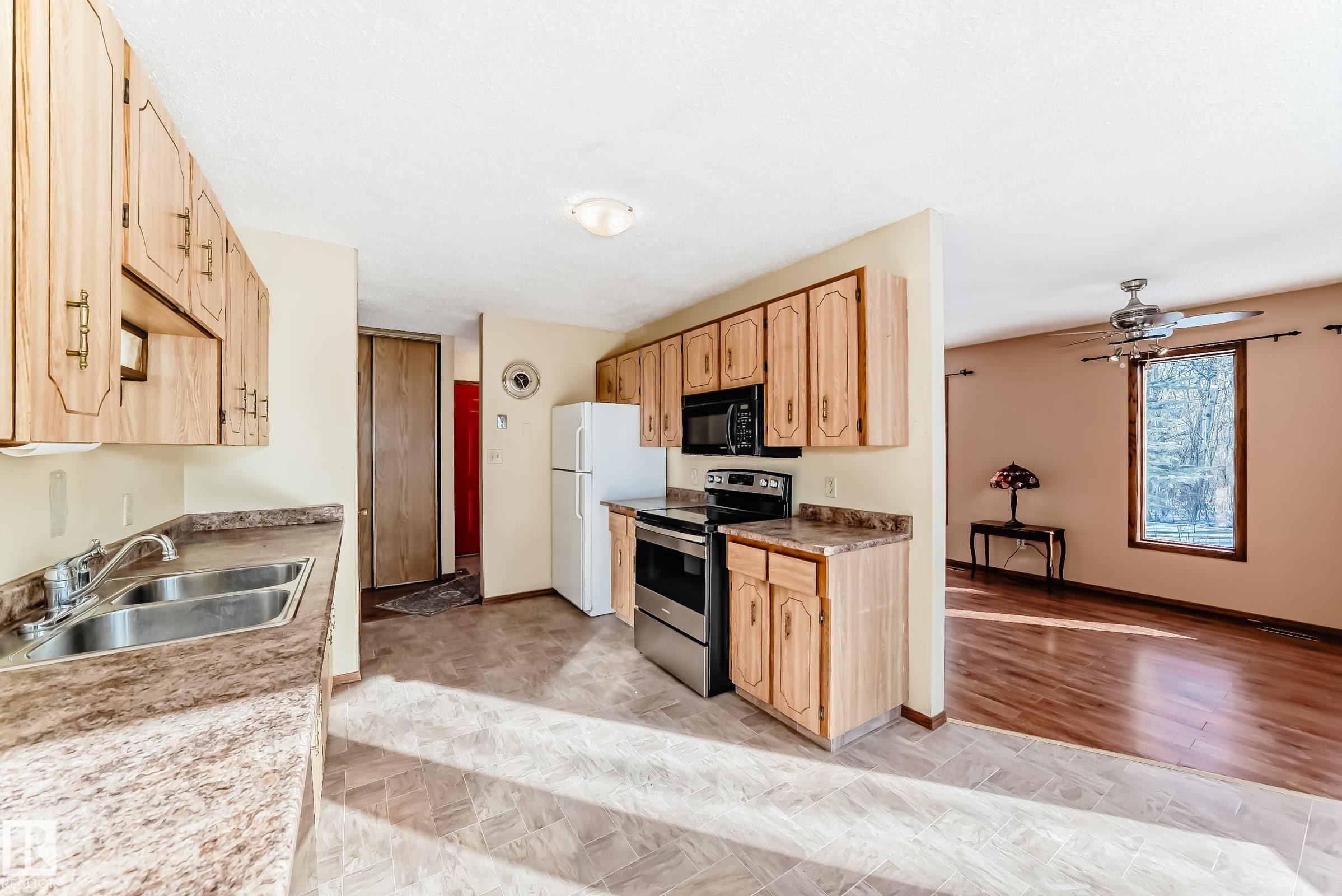 The kitchen features light wood cabinetry, a double basin stainless steel sink, and stainless steel appliances including a microwave and oven - 100 23016 Twp Rd 504, Rural Leduc County, AB - Indoor Photo Showing Kitchen With Double Sink