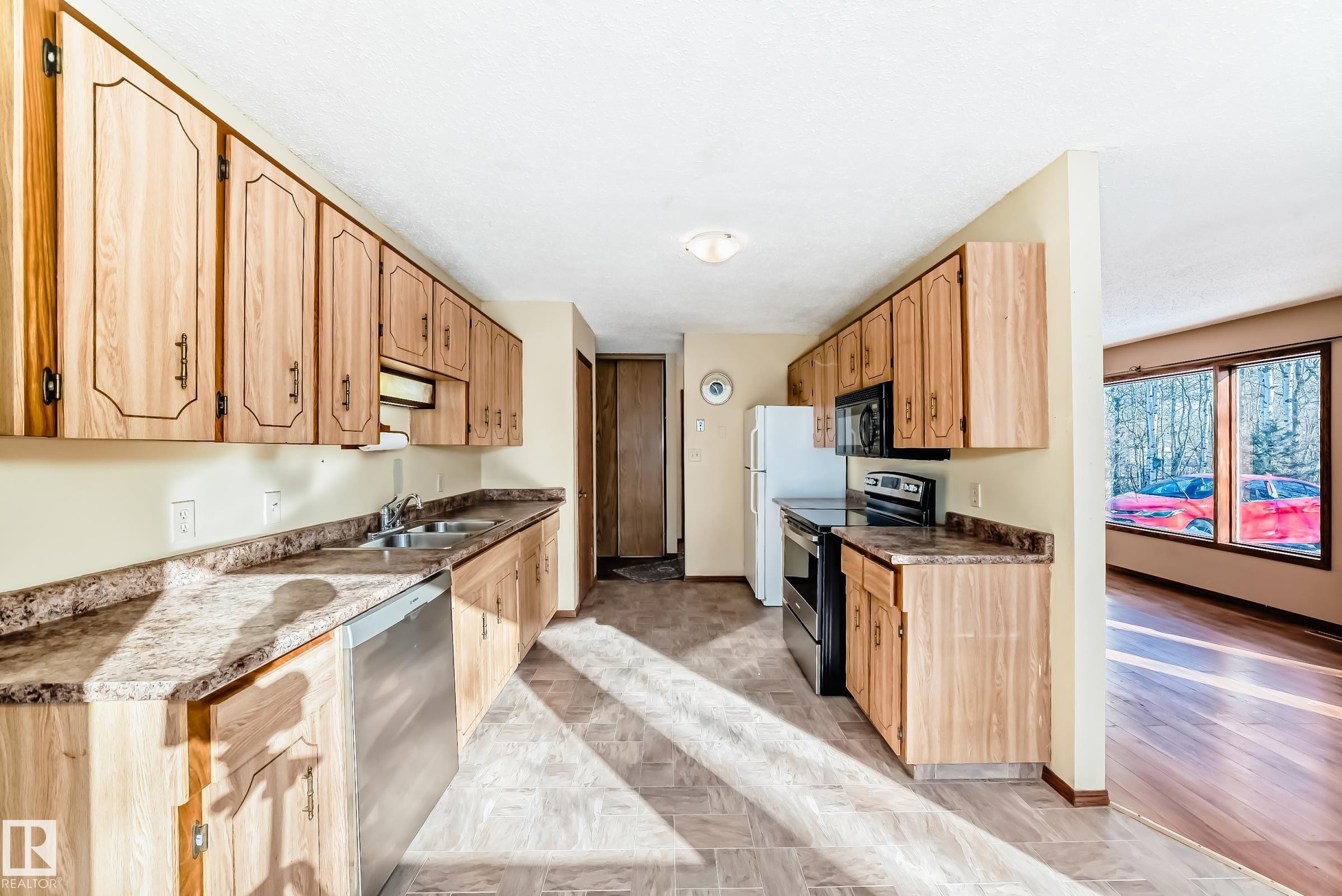 The kitchen features wood cabinetry, a double basin sink, and a dishwasher - 100 23016 Twp Rd 504, Rural Leduc County, AB - Indoor Photo Showing Kitchen With Double Sink
