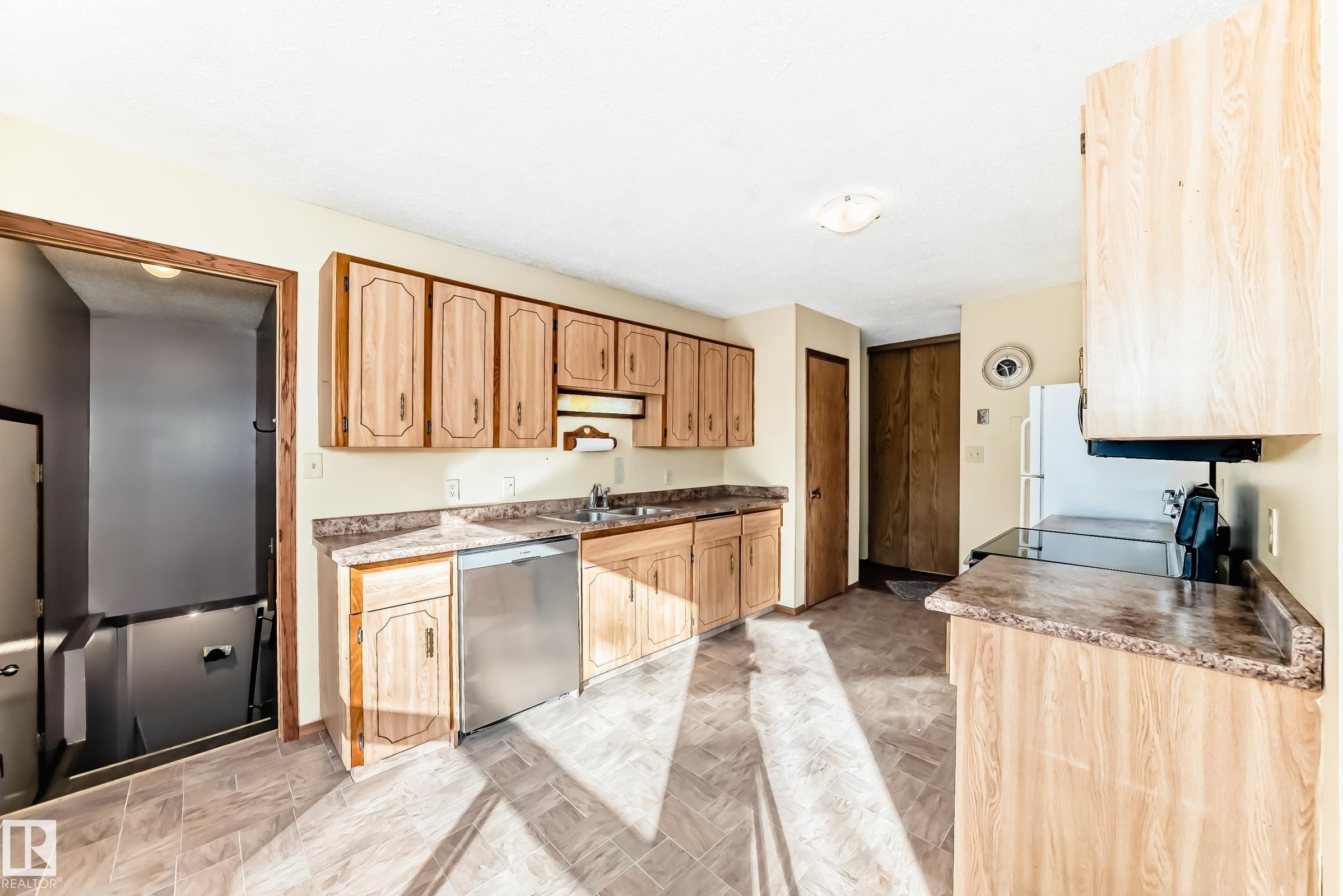 The kitchen features wood cabinetry, a stainless steel dishwasher, and a refrigerator - 100 23016 Twp Rd 504, Rural Leduc County, AB - Indoor Photo Showing Kitchen