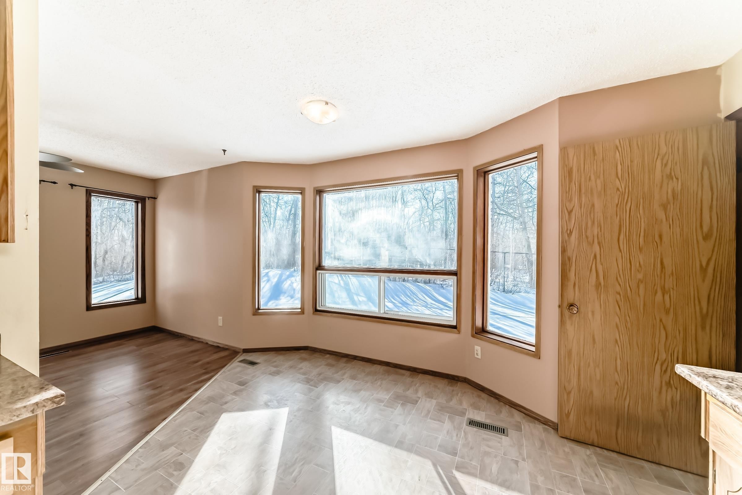 This bright living area features a bay window design with wood trim, providing expansive views of the outdoors - 100 23016 Twp Rd 504, Rural Leduc County, AB - Indoor Photo Showing Other Room