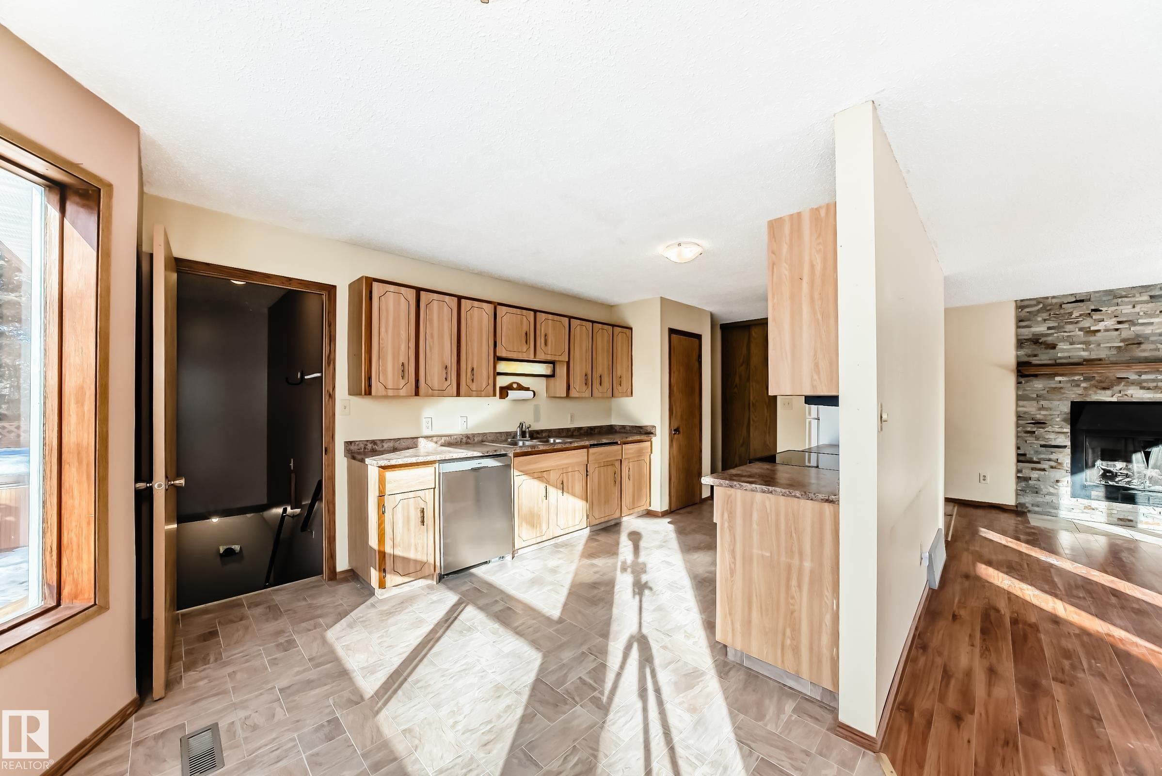 The kitchen features wood cabinetry, a stainless steel dishwasher, and a window providing natural light - 100 23016 Twp Rd 504, Rural Leduc County, AB - Indoor Photo Showing Kitchen
