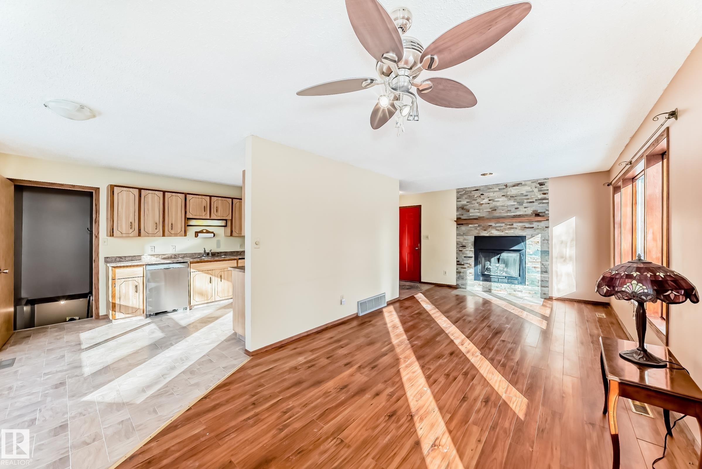 The living area features wood flooring, a stone fireplace, and a ceiling fan - 100 23016 Twp Rd 504, Rural Leduc County, AB - Indoor With Fireplace