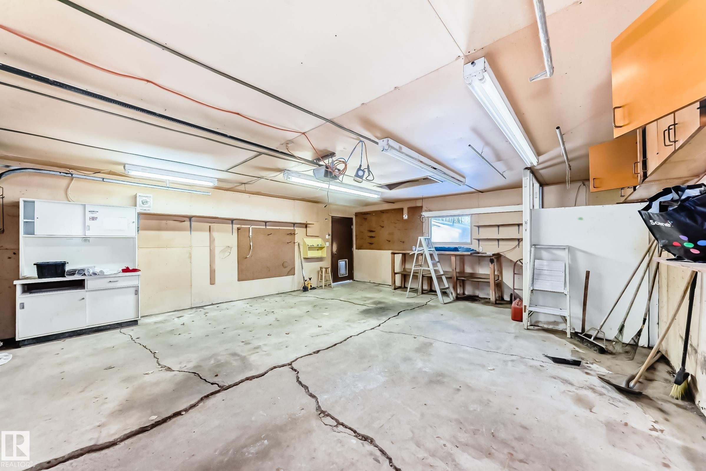 The property includes a spacious garage with a concrete floor, equipped with overhead fluorescent lighting and wall-mounted storage cabinets - 100 23016 Twp Rd 504, Rural Leduc County, AB - Indoor Photo Showing Garage