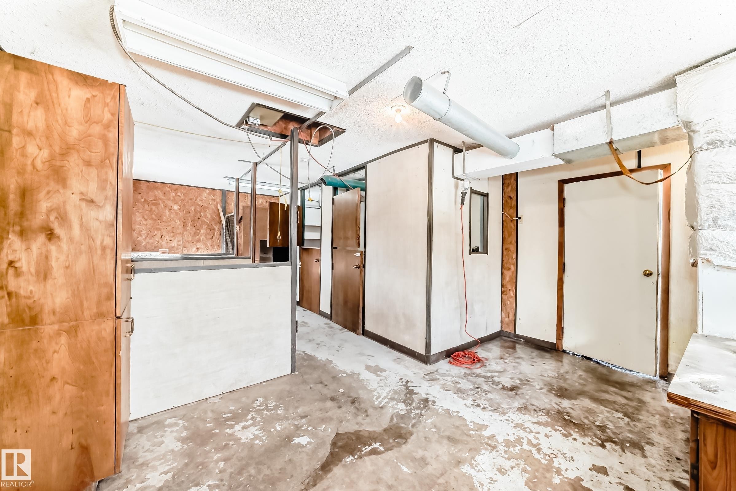 Unfinished interior space featuring exposed ceiling pipes, concrete flooring, and wooden cabinetry - 100 23016 Twp Rd 504, Rural Leduc County, AB -