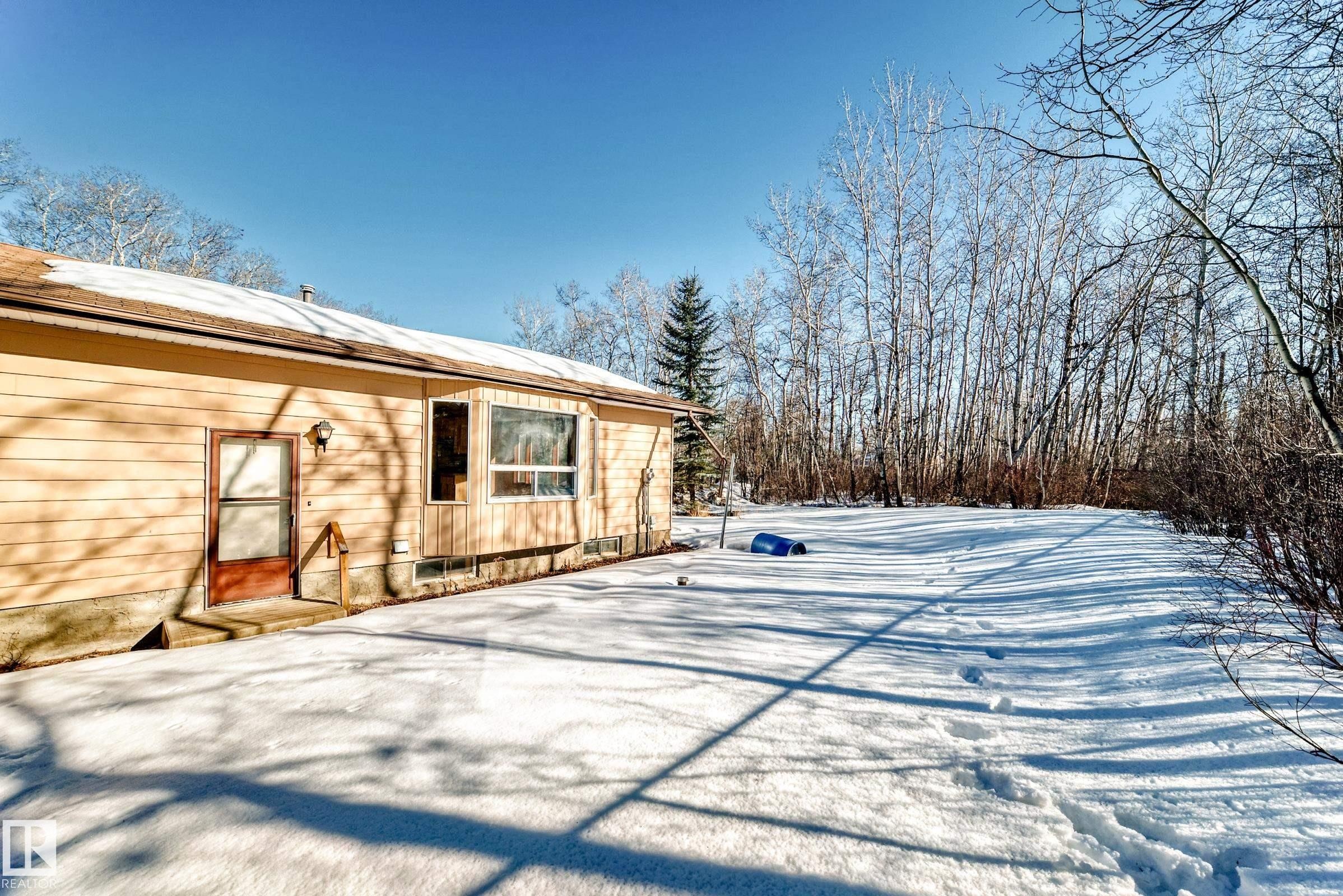 The property features a light-colored exterior with a brown door and a bay window - 100 23016 Twp Rd 504, Rural Leduc County, AB - Outdoor