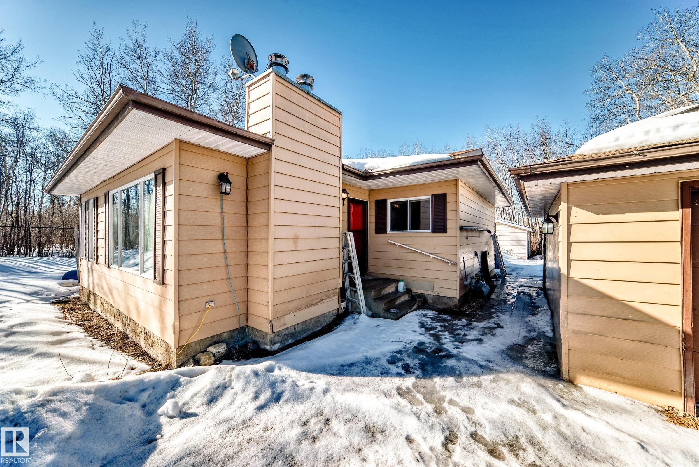 The property features light-colored horizontal siding, a brown roof, and multiple windows - 100 23016 Twp Rd 504, Rural Leduc County, AB - Outdoor With Exterior
