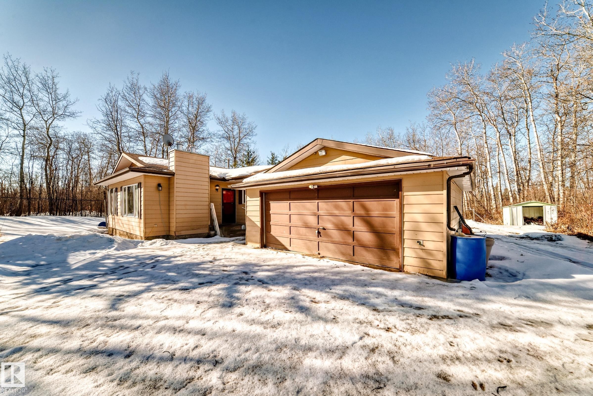 The property features a tan exterior with a brown garage door - 100 23016 Twp Rd 504, Rural Leduc County, AB - Outdoor