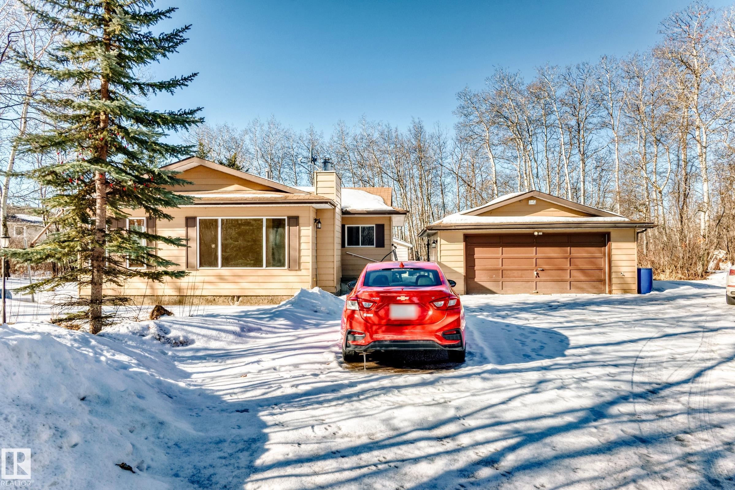 The property features a detached garage with a brown garage door, a light-colored exterior, and an expansive driveway - 100 23016 Twp Rd 504, Rural Leduc County, AB - Outdoor