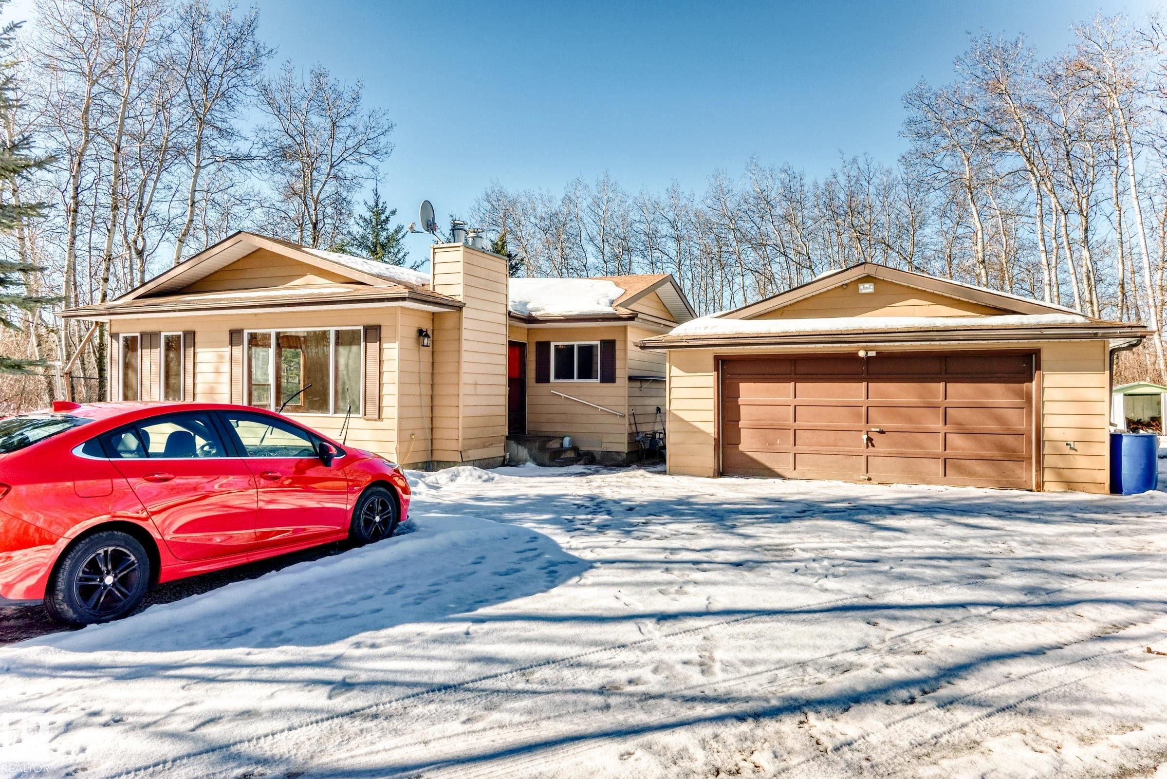 The property features a single-story residence with a light-colored exterior and a detached two-car garage with a brown door - 100 23016 Twp Rd 504, Rural Leduc County, AB - Outdoor