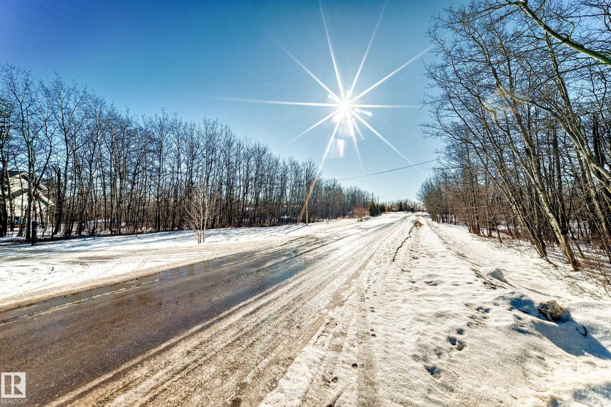 This property is located on a road with snow-covered verges and a clear, blue sky overhead - 100 23016 Twp Rd 504, Rural Leduc County, AB - Outdoor With View