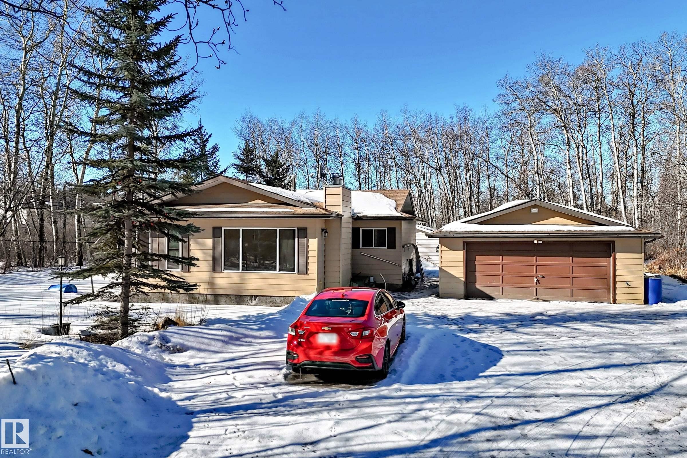 The property features a ranch-style home with a detached garage, set against a backdrop of bare trees - 100 23016 Twp Rd 504, Rural Leduc County, AB - Outdoor