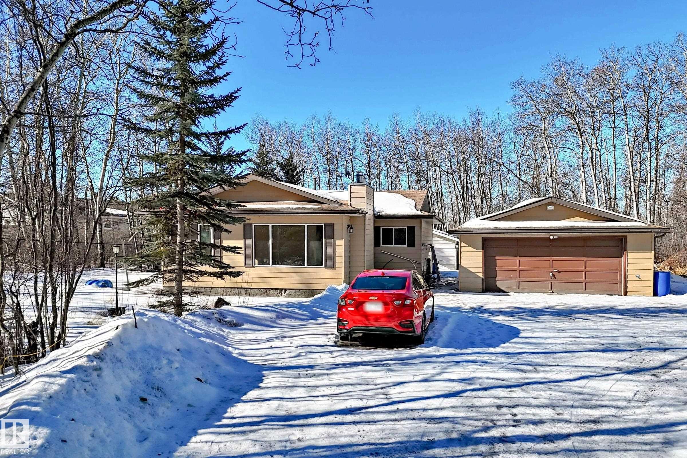 The property features a detached garage with a brown door, a driveway, and a front facade with a large window - 100 23016 Twp Rd 504, Rural Leduc County, AB - Outdoor