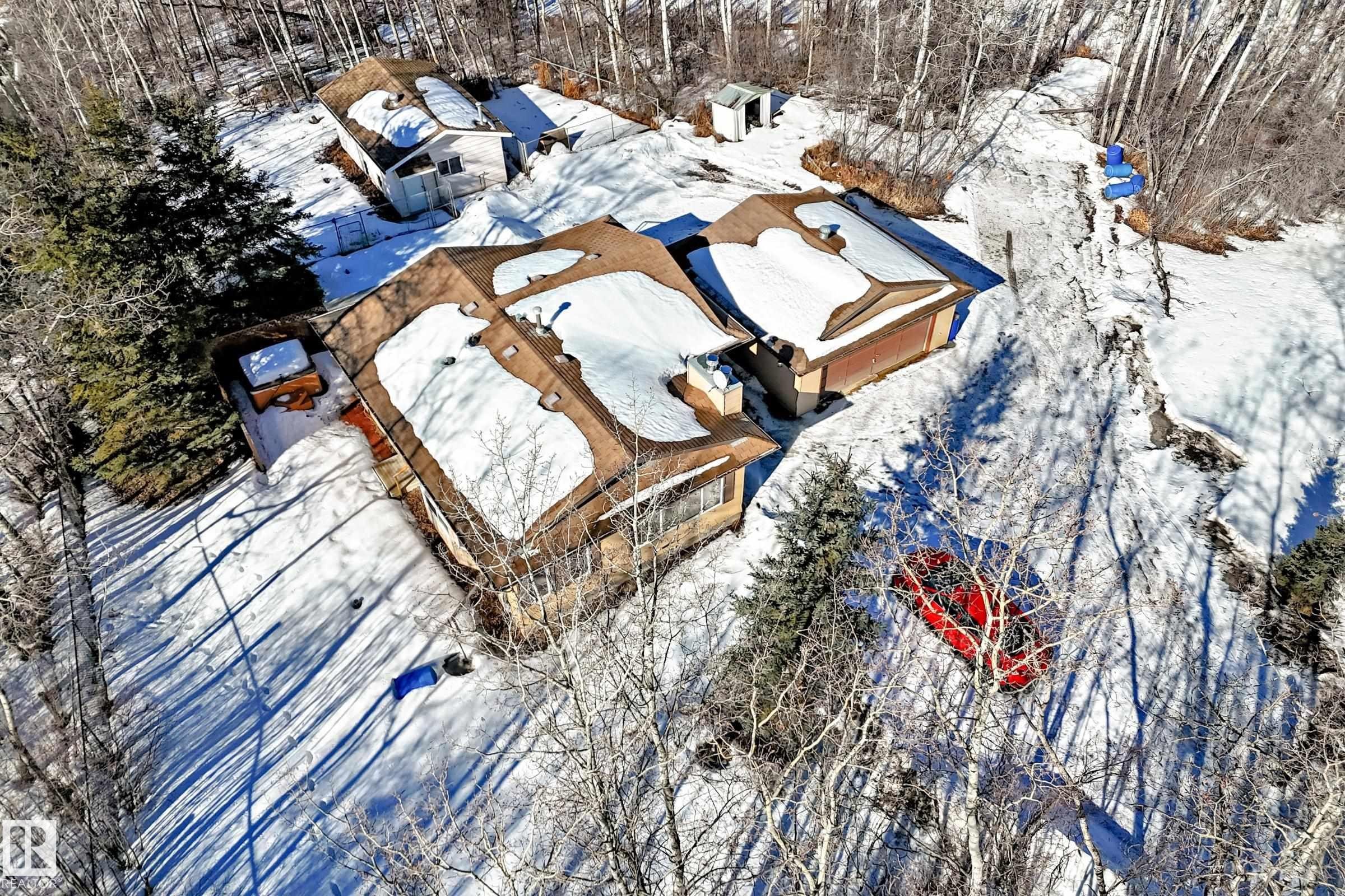Aerial view of the property showing multiple structures with snow-covered roofs, surrounded by trees - 100 23016 Twp Rd 504, Rural Leduc County, AB - Outdoor