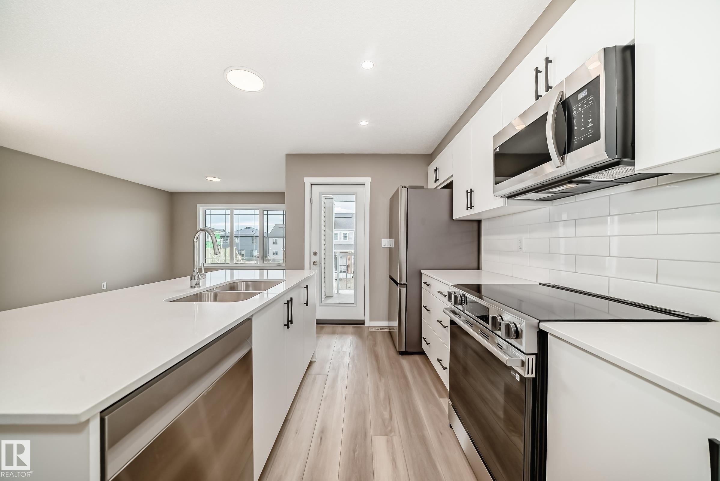 Modern kitchen featuring white cabinetry with matte black hardware, stainless steel appliances, and a large island with an undermount double sink - 20415 16 Avenue, Edmonton, AB