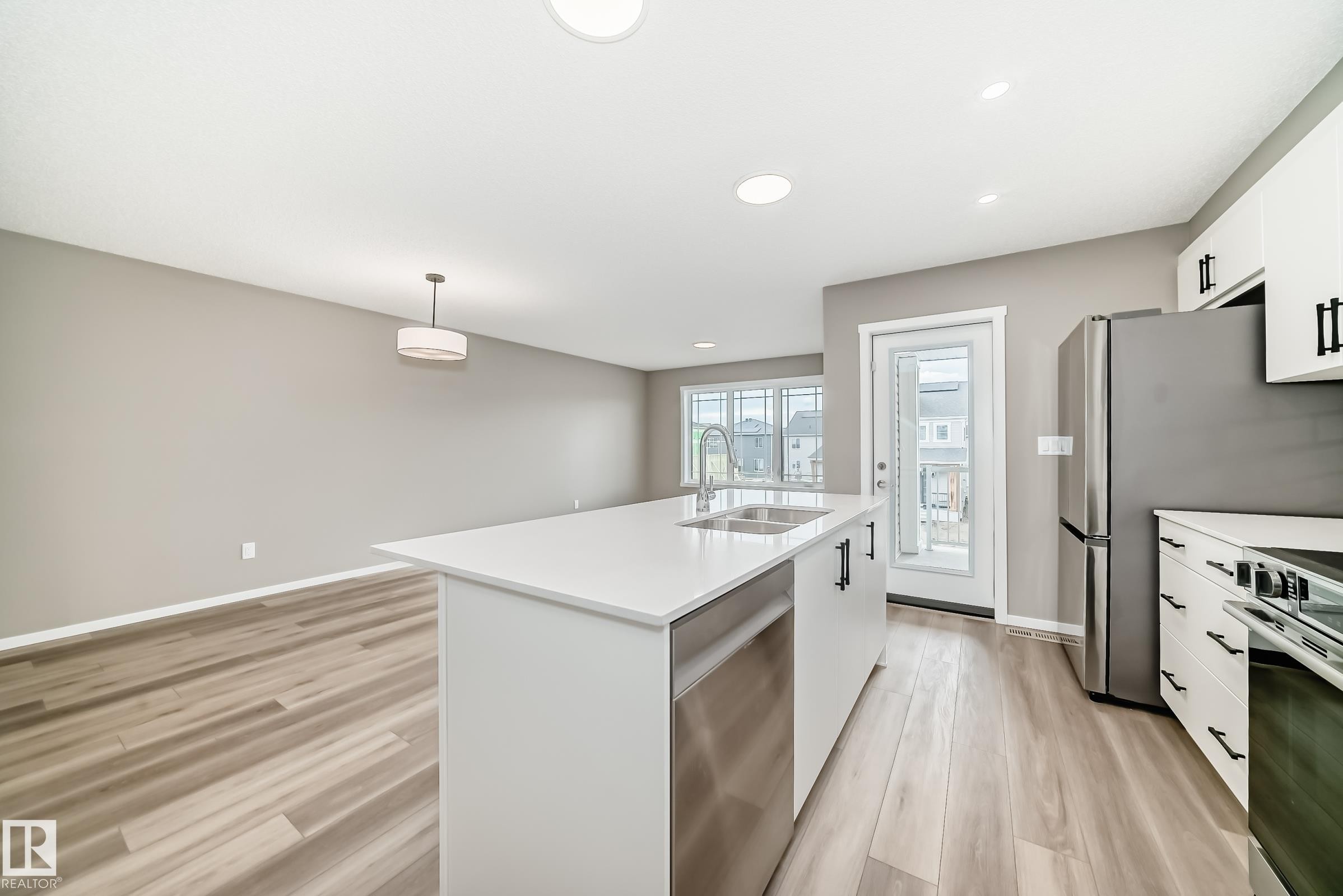 Open-concept kitchen featuring a large island with white countertops, stainless steel sink, and integrated dishwasher - 20415 16 Avenue, Edmonton, AB