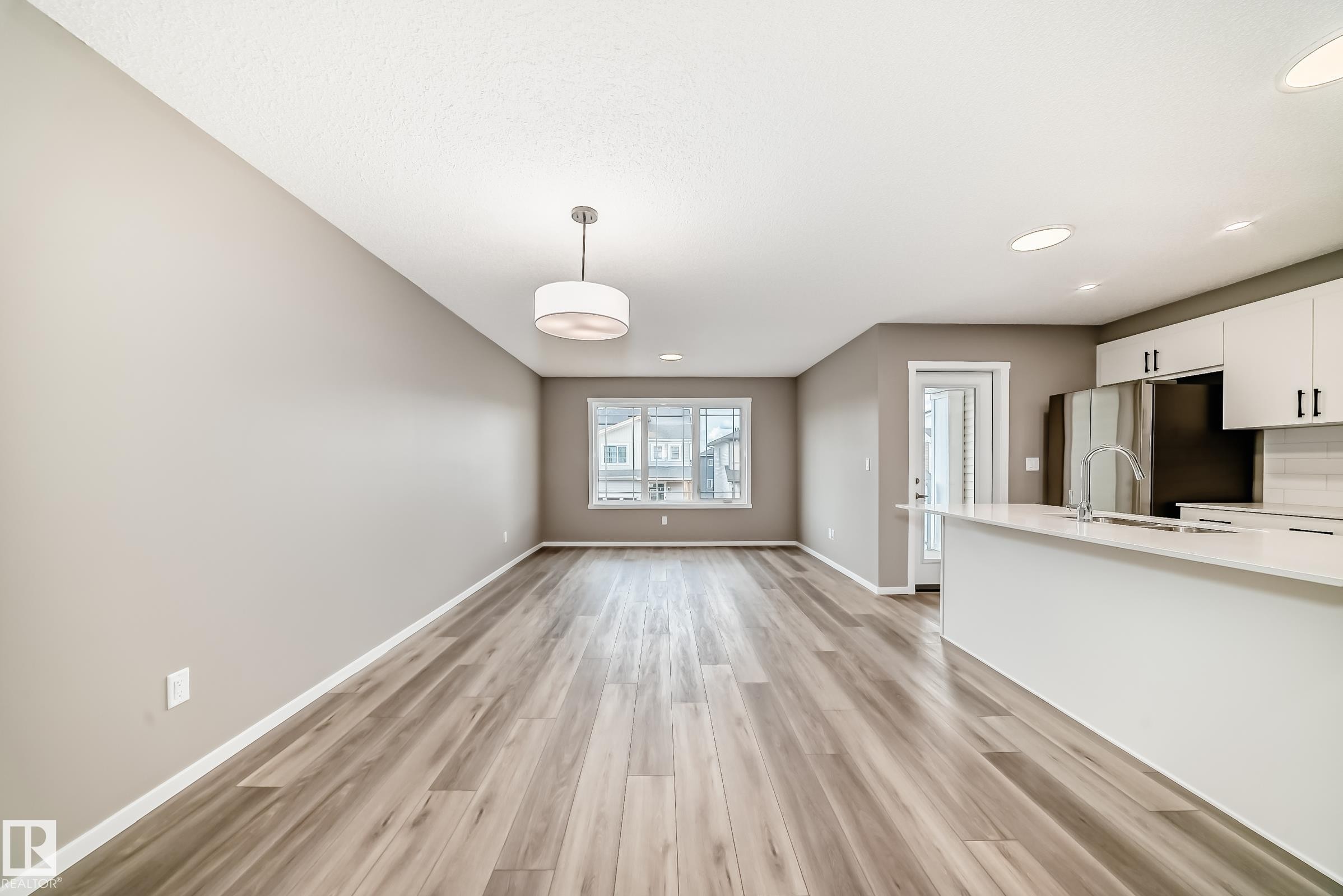 Open-concept living area featuring wood-finish flooring, a modern chandelier, and a kitchen island with an undermount sink - 20415 16 Avenue, Edmonton, AB