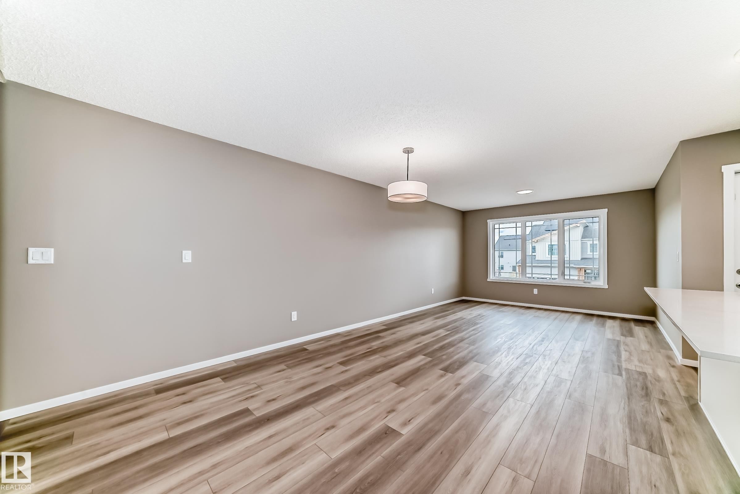 Open living space featuring wood-finish flooring, neutral-toned walls, and a contemporary ceiling light fixture - 20415 16 Avenue, Edmonton, AB