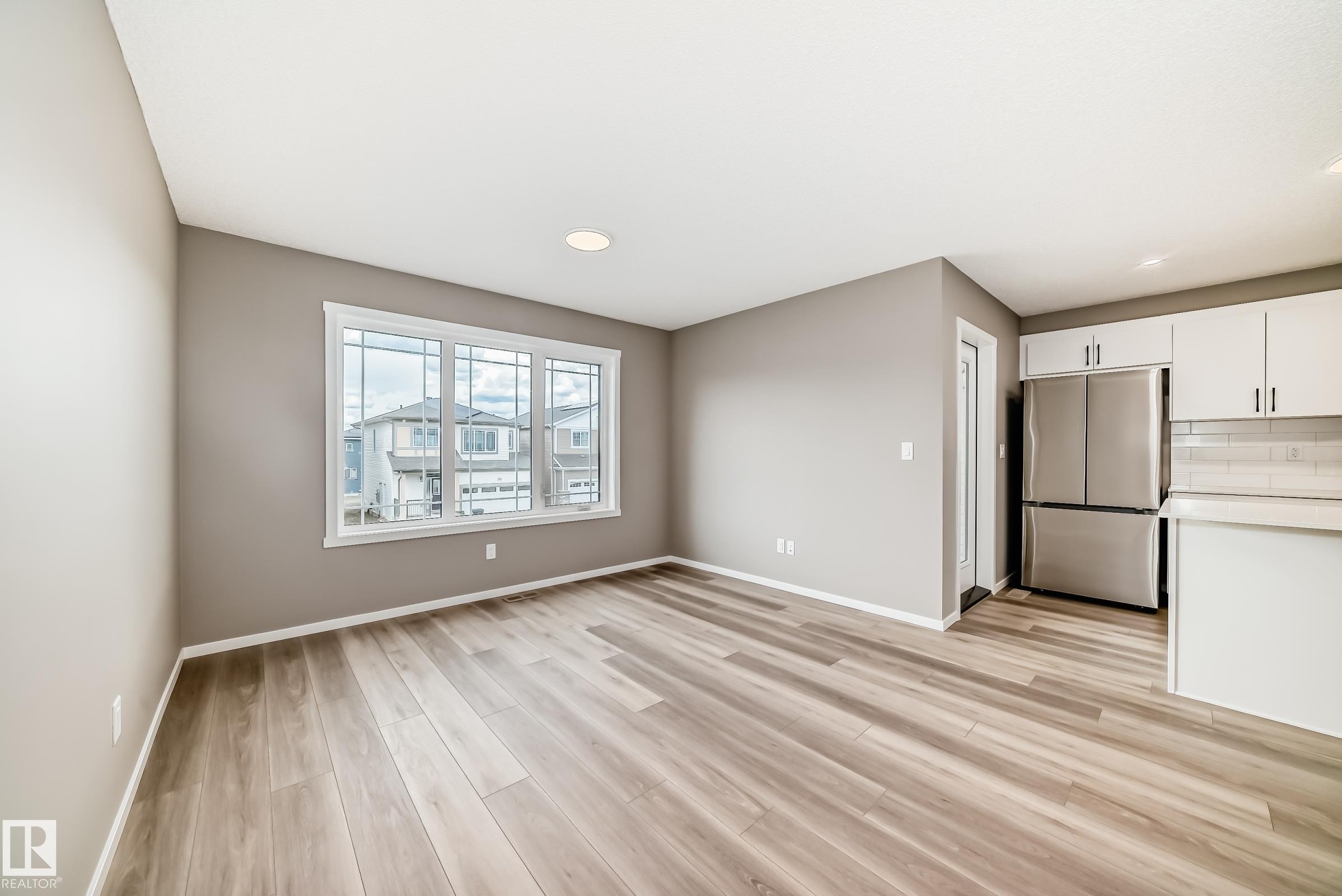 Open-concept living area with wood-finish flooring, a large multi-pane window, and recessed lighting - 20415 16 Avenue, Edmonton, AB