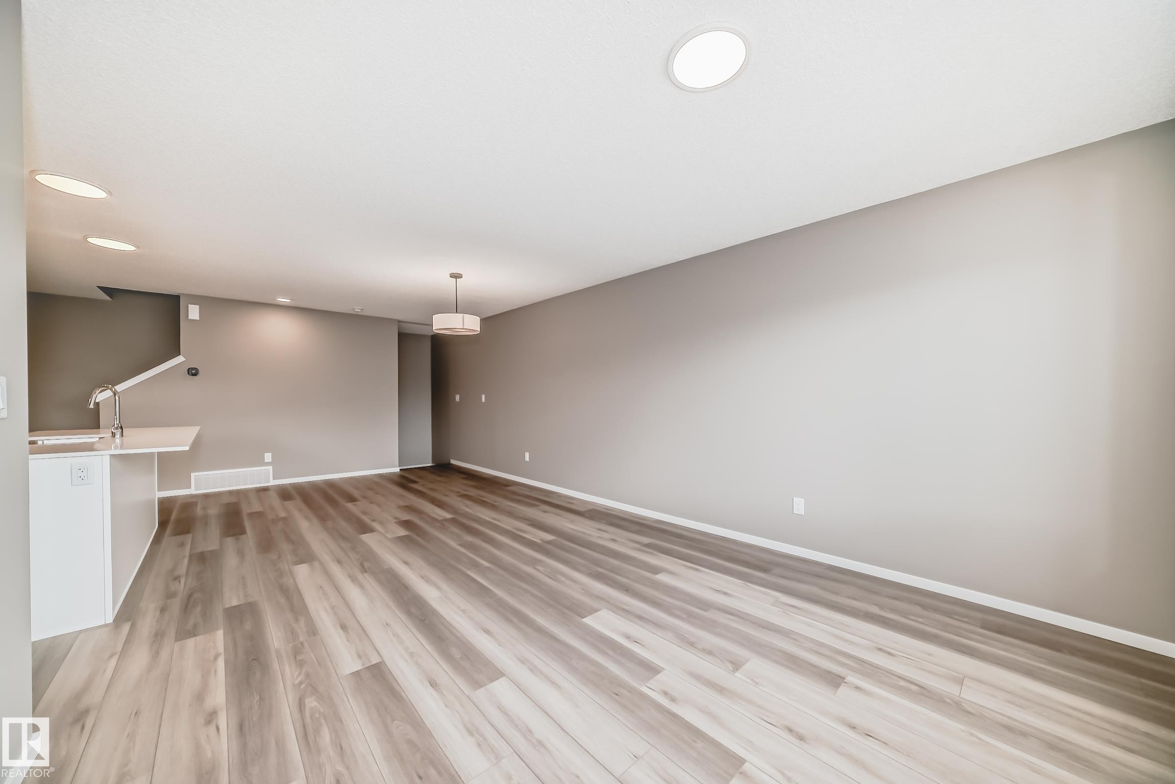 Spacious room featuring wood-finish flooring, recessed lighting, and a contemporary pendant light fixture - 20415 16 Avenue, Edmonton, AB