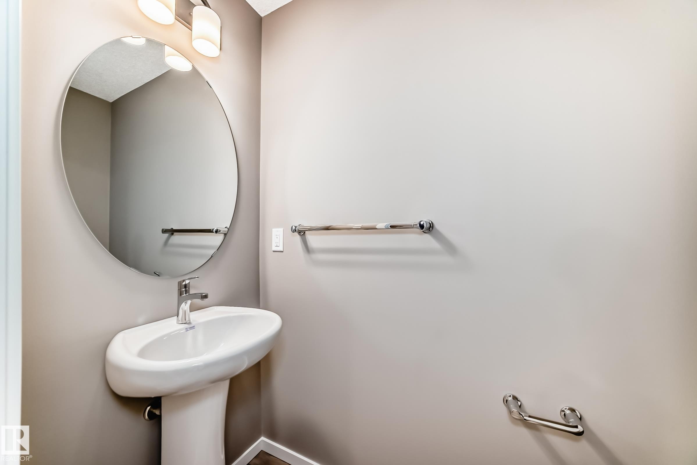 Pedestal sink with a polished chrome faucet, complemented by a round wall-mounted mirror - 20415 16 Avenue, Edmonton, AB