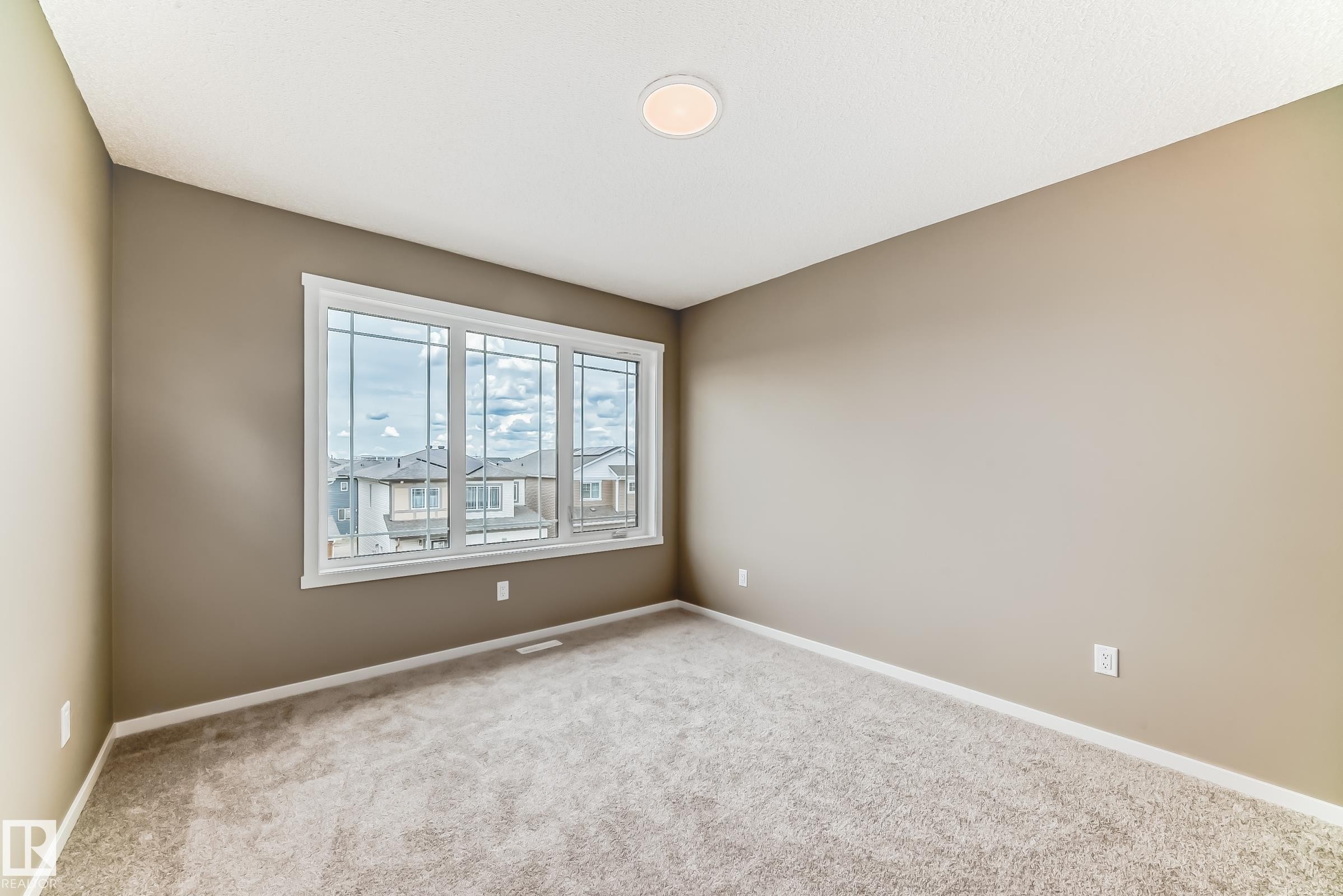 Spacious room featuring a large triple-pane window with white trim, neutral-toned carpeting, and light brown wall paint - 20415 16 Avenue, Edmonton, AB