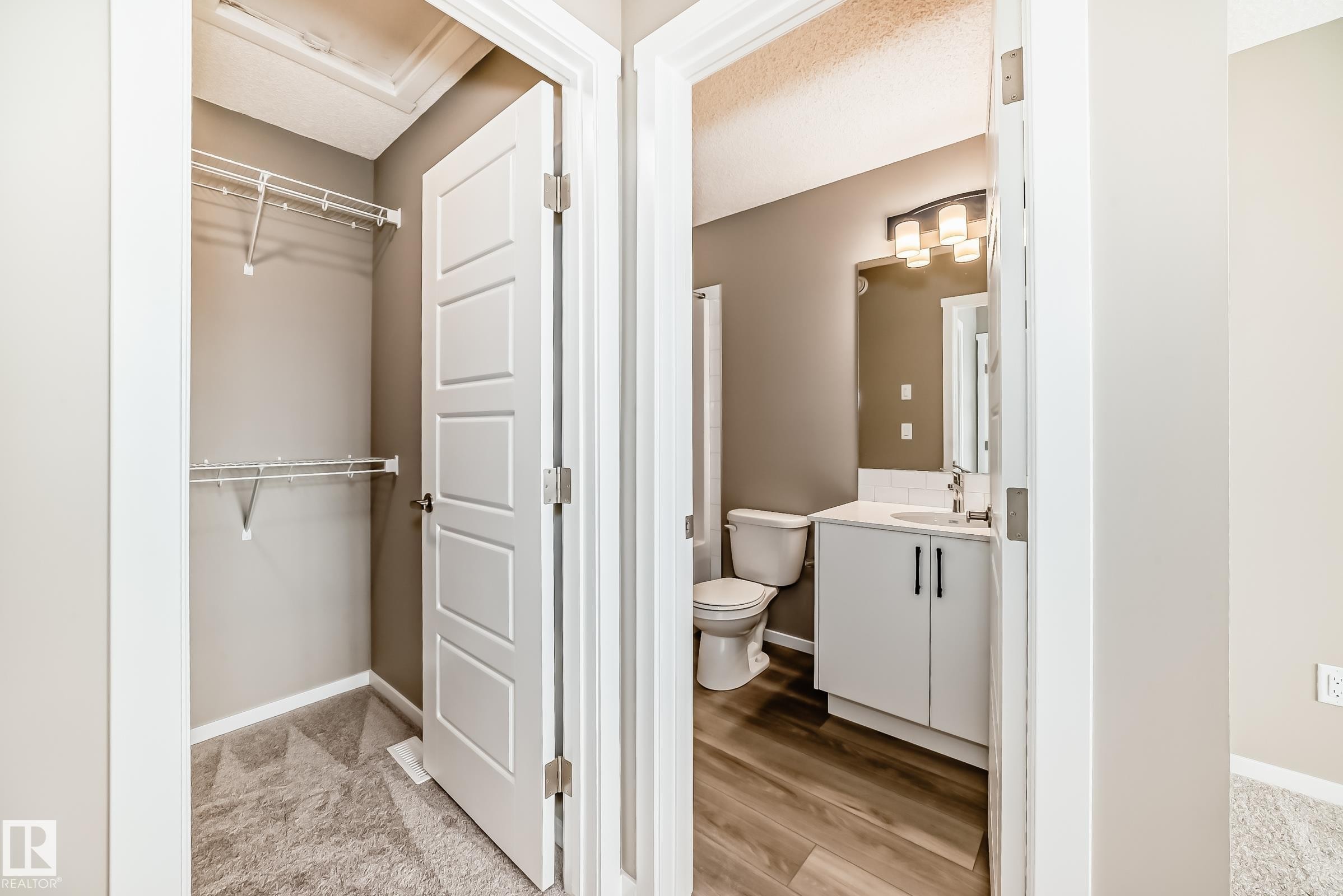 Modern bathroom featuring a white vanity with dark hardware, a rectangular mirror, and wood-finish flooring - 20415 16 Avenue, Edmonton, AB