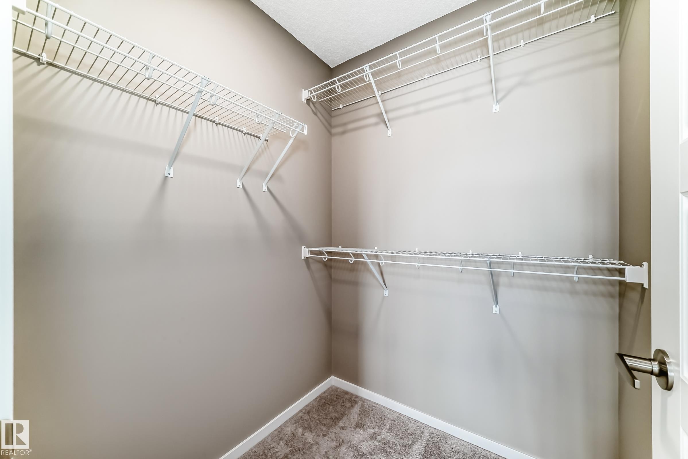 Walk-in closet featuring neutral-toned walls, white wire shelving, white trim, and textured carpet flooring - 20415 16 Avenue, Edmonton, AB