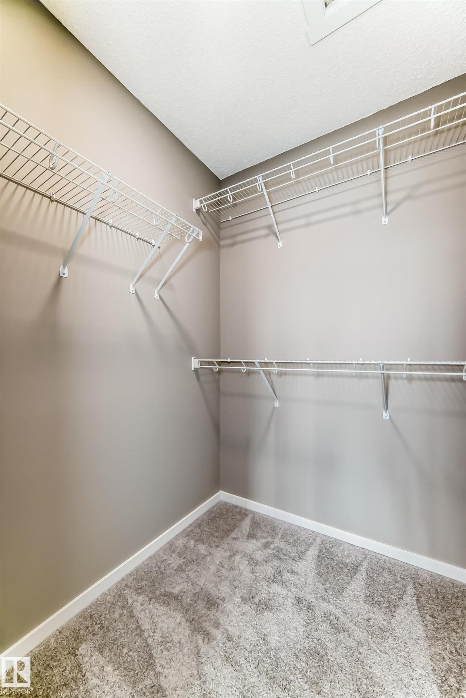 Walk-in closet featuring wire shelving, wall-mounted hanging rods, light gray wall paint, white baseboards, and gray carpet flooring - 20415 16 Avenue, Edmonton, AB