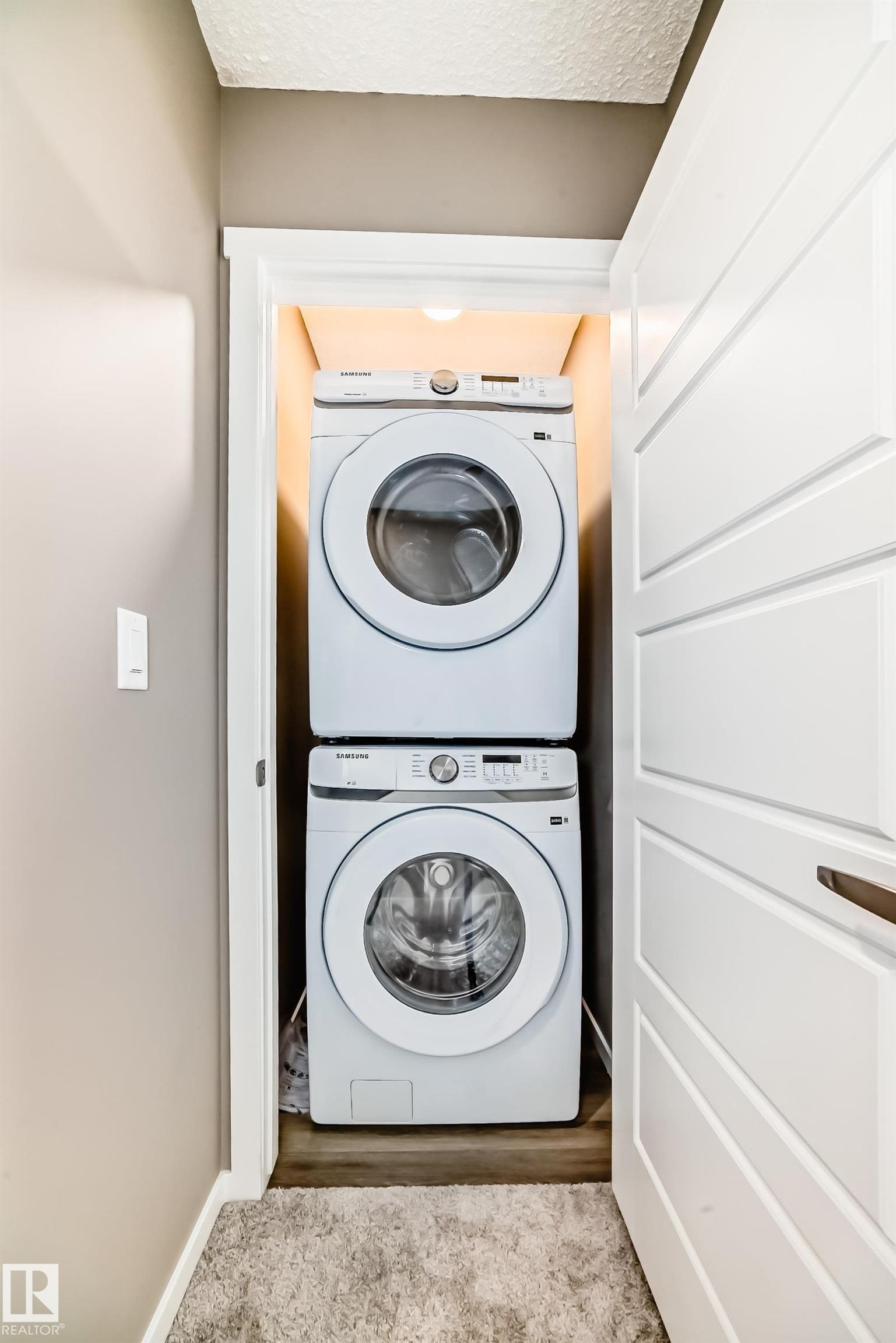 Stackable laundry units within a dedicated closet space, featuring wood-finish flooring and integrated overhead lighting - 20415 16 Avenue, Edmonton, AB